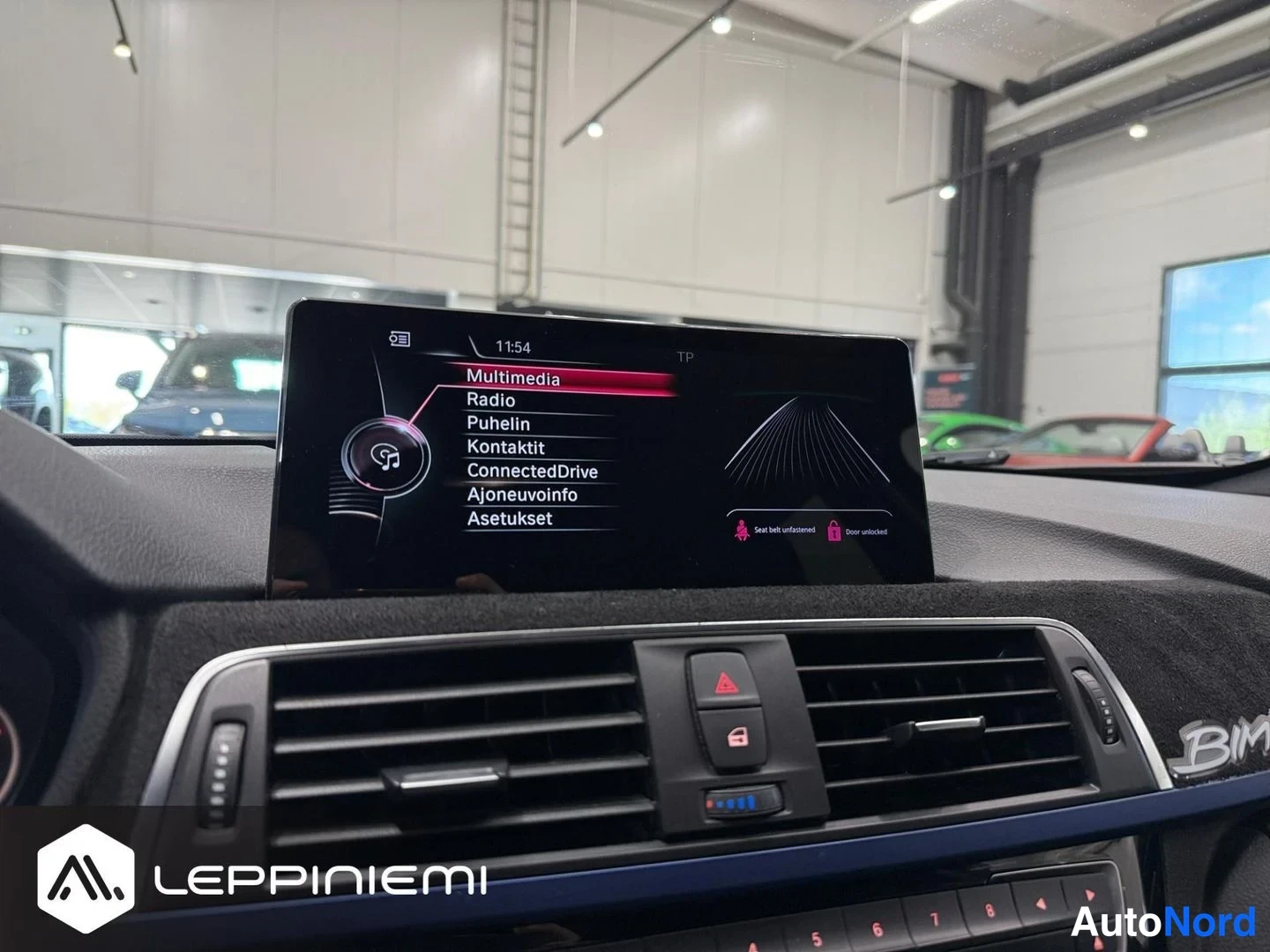 Muu: Kojelaudan medianäyttö käynnissä: valikossa vaihtoehdot Multimedia, Radio, Puhelin, Kontaktit, ConnectedDrive, Ajoneuvoinfo ja Asetukset, kello 11:54.