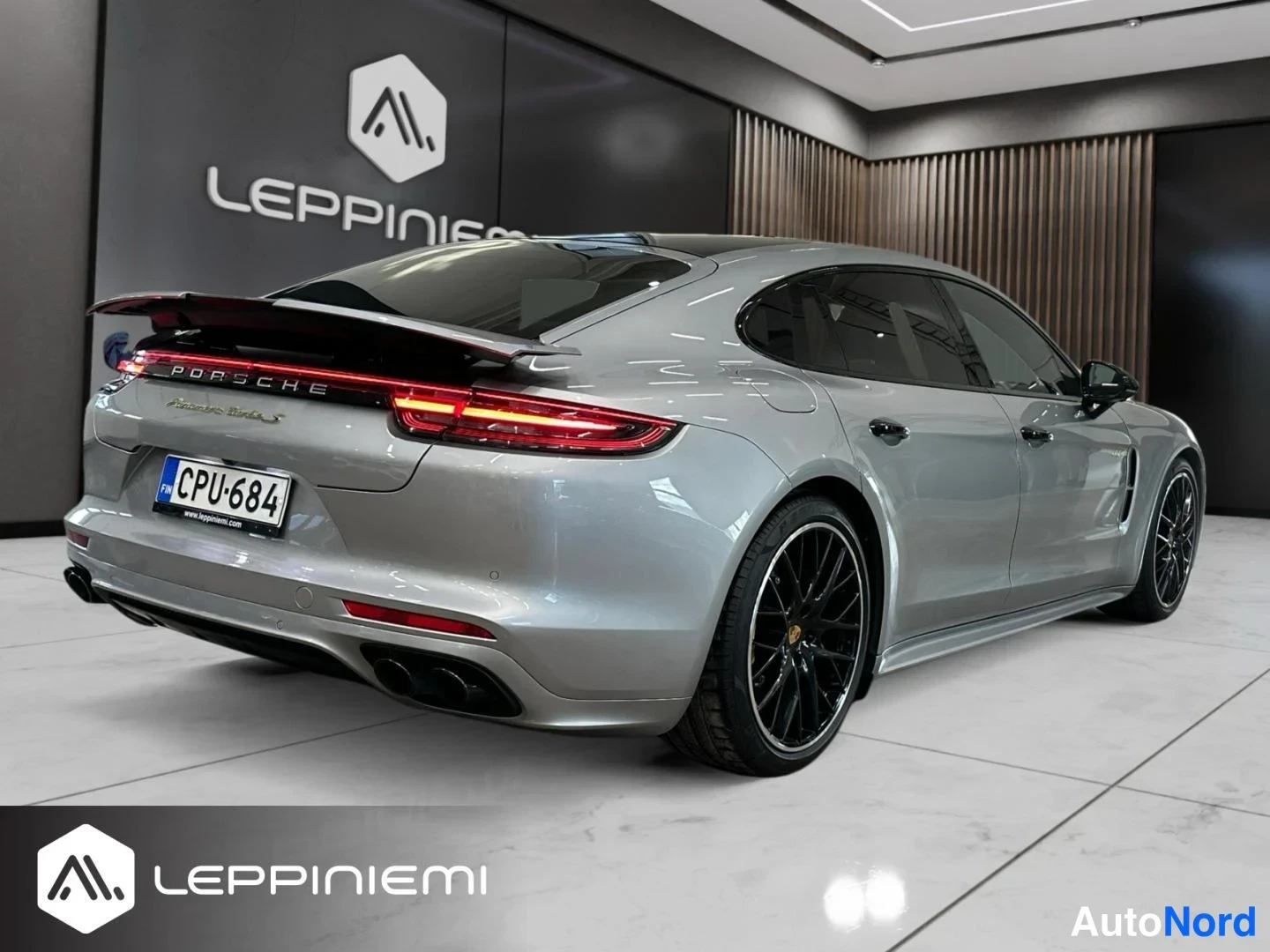 Takaviisto: Porsche Panamera -auton takakulma: hopeakarmea yhtye, rekisterikilpi, mustat kevytmetallivanteet ja PORSCHE-teksti takavalossa.