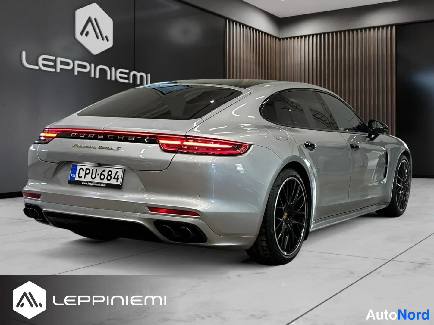 Takaviisto: Porsche Panamera -auton takakulma sisätiloissa: hopeakarmea yhtye, takavalot päällä, rekisterikilpi, mustat vanteet.