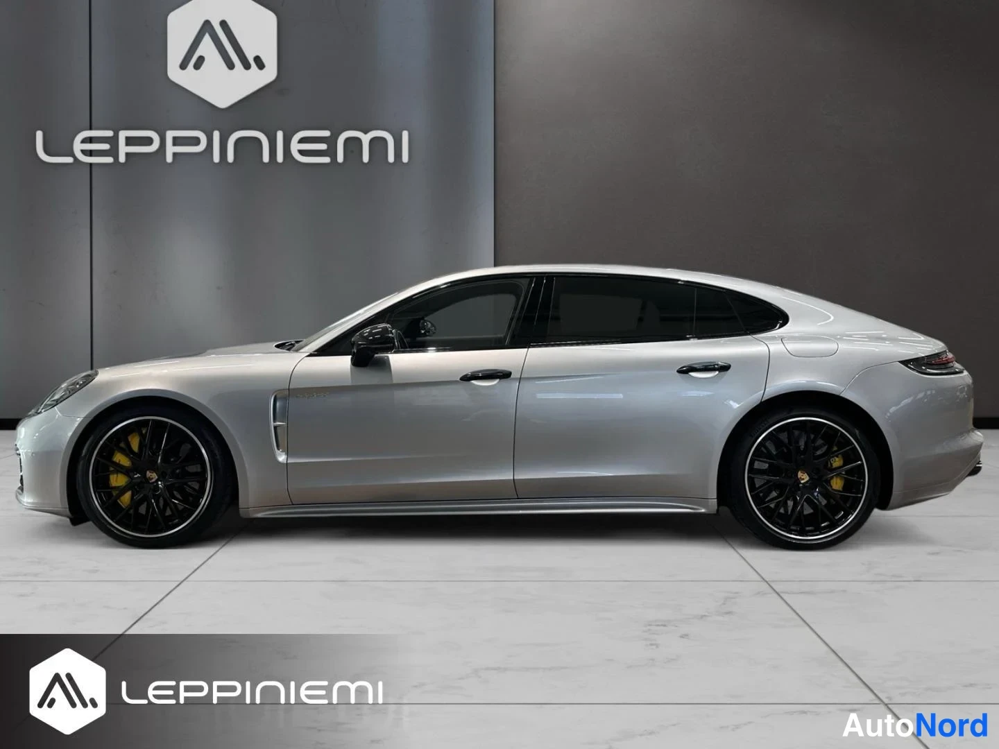 Sivulta: Porsche Panamera -sedanin sivuprofiili studiossa, hopeinen koriväri, mustat alumiinivanteet ja keltaiset jarrusatulat.