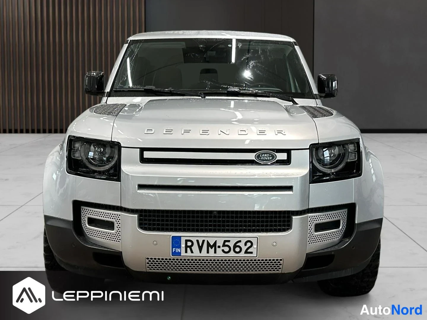 Edestä: Land Rover Defenderin suora etukuva, DEFENDER-teksti konepellillä, LAND ROVER-merkki säleikössä ja rekisteritunnus.