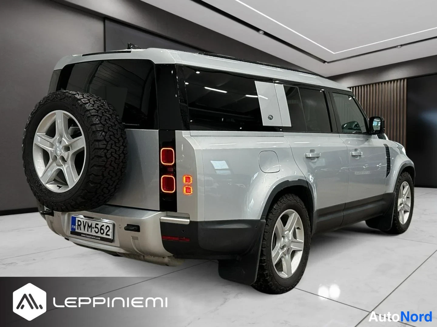 Takaviisto: Land Rover Defenderin takaosan kolmasosa vasemmalta: varaossa pyöränkansi ja rekisterikilpi, hopeanvärinen kori ja tummat ikkunat autonäyttelyssä.
