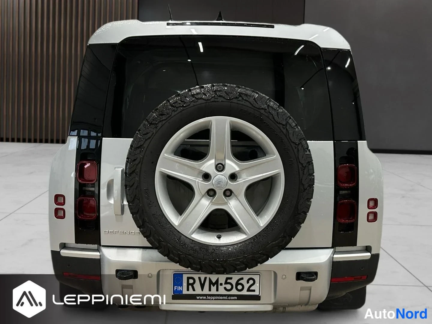 Takaa: Land Rover Defender suoraan takaa: varaossa pyörä, DEFENDER-teksti ja rekisterikilpi autonäyttelyssä.