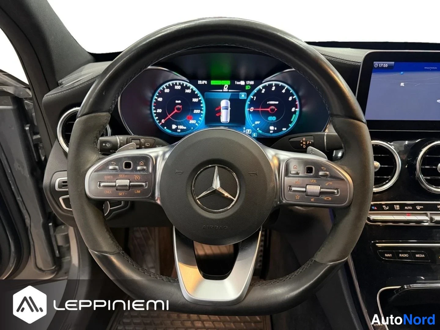 Yksityiskohta: Mercedes-Benzin ohjaamo: mittaristö ja multitoimintoinen ohjauspyörä, keskinäyttö näyttää kartan ja kellonajan 17:55.