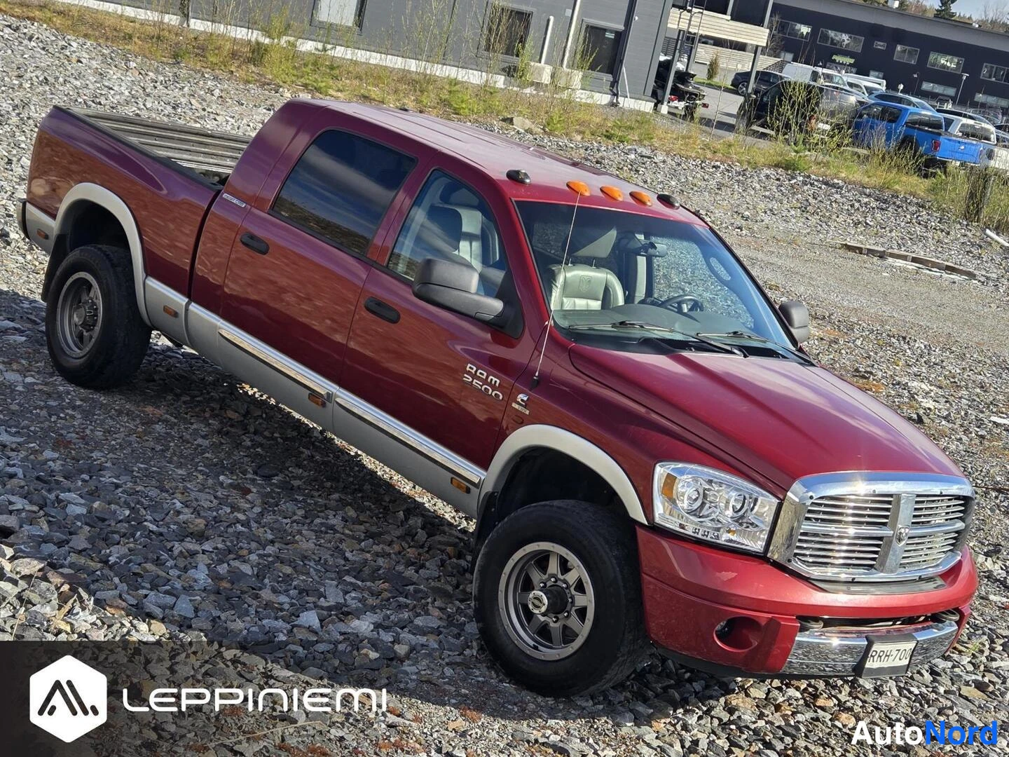 Etuviisto, nokka oikealle: Punainen Dodge Ram 2500 -nákkuauto etuviistokuva oikealta, avolata näkyy takana, auto kivikkoisella pihamaalla.