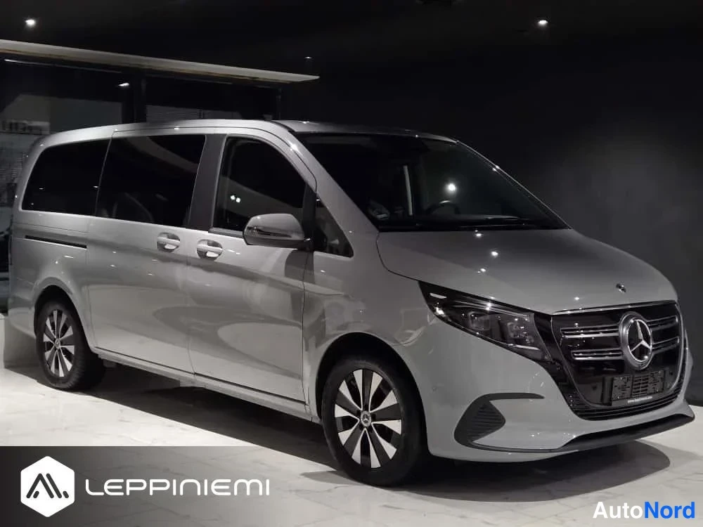 Etuviisto, nokka oikealle: Mercedes-Benz EQV -pakettiauto sivusta-etukulmasta, keula oikealla, hopeanharmaassa näyttelytilassa.