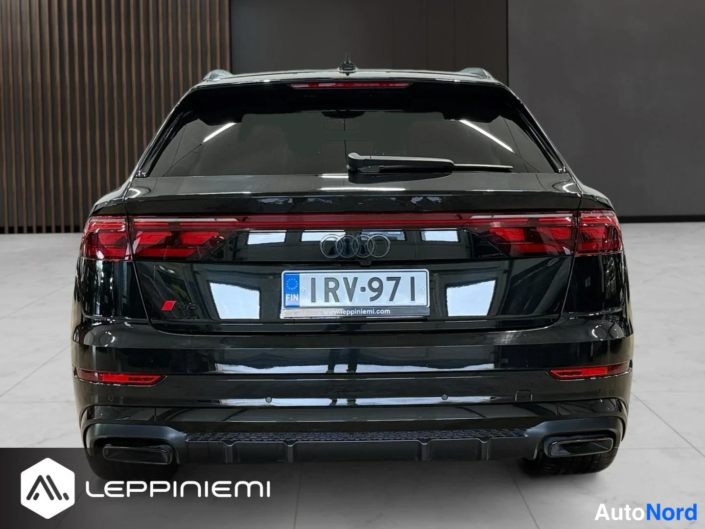 Takaa: Mustan Audi-suvun takaosa; punaiset takavalot, Audi-renkaiden logo, rekisterikilpi ja kaksi pakoputkea.