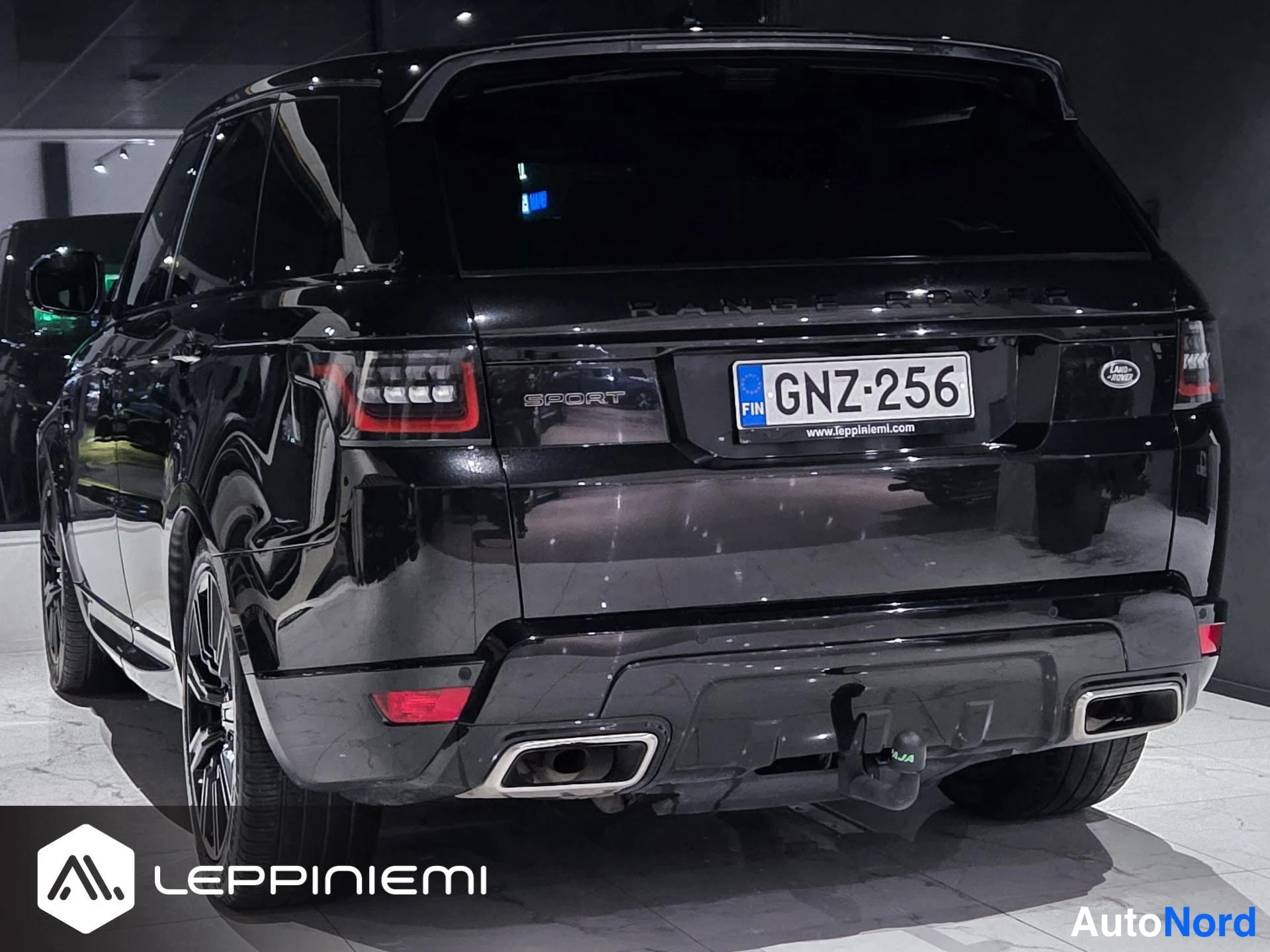 Takaviisto: Mustan Range Rover Sportin takaosa ja vasen kylki kolmostakakulmasta; rekisteritunnus, takana kaarrebyssä.