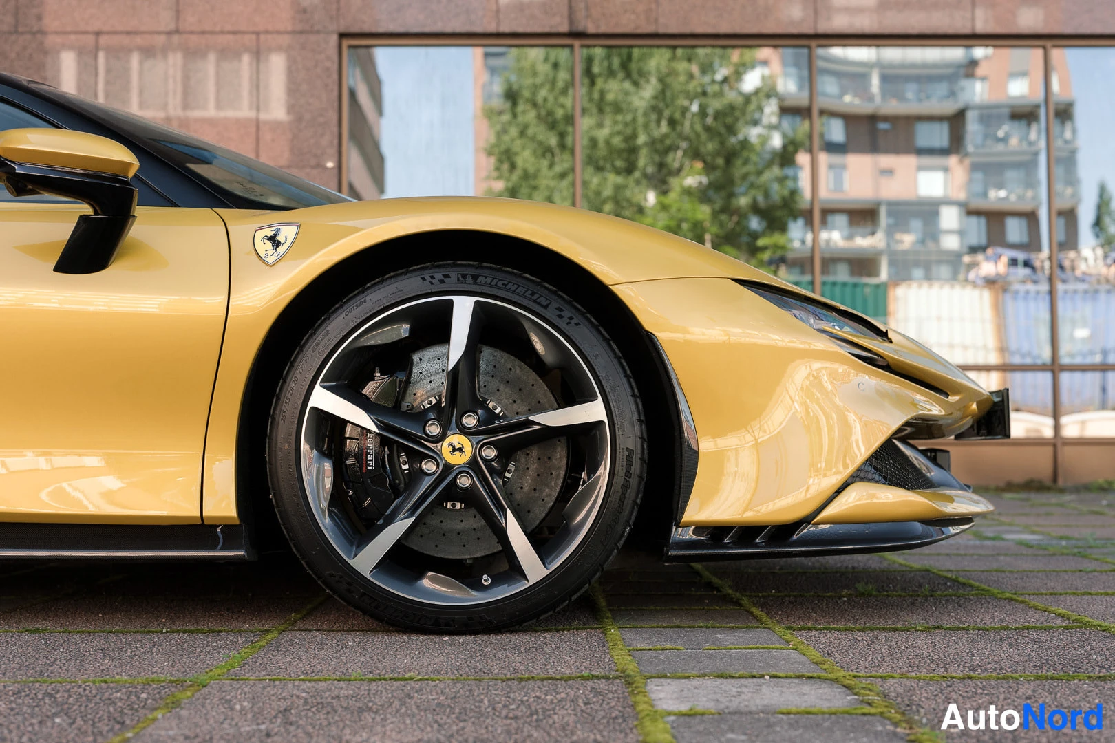 Etuviisto, nokka oikealle: Keltaisen auton etupyörän lähikuva, viisisakarainen hopea-musta vannemusta ja Ferrari-merkki.