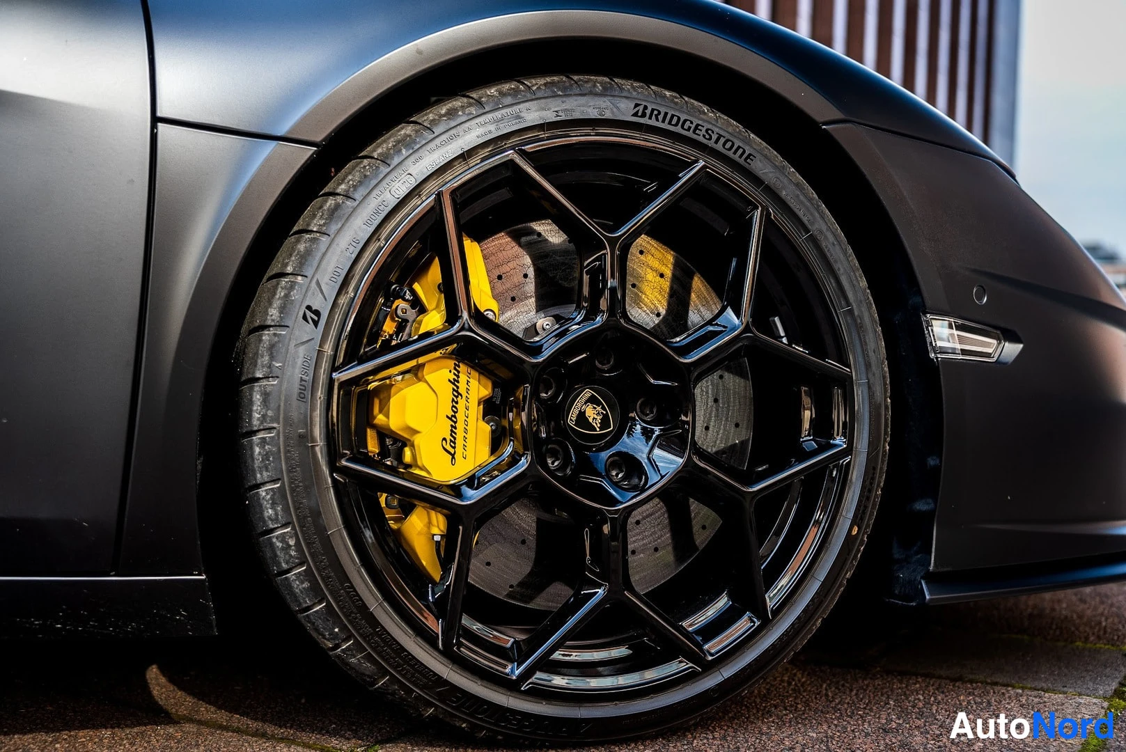 Sivulta: Mustan auton etupyörän lähikuva: musta vanteen kevytmetallivanne, keltainen Lamborghini-jarrusatula ja Bridgestone-renkas