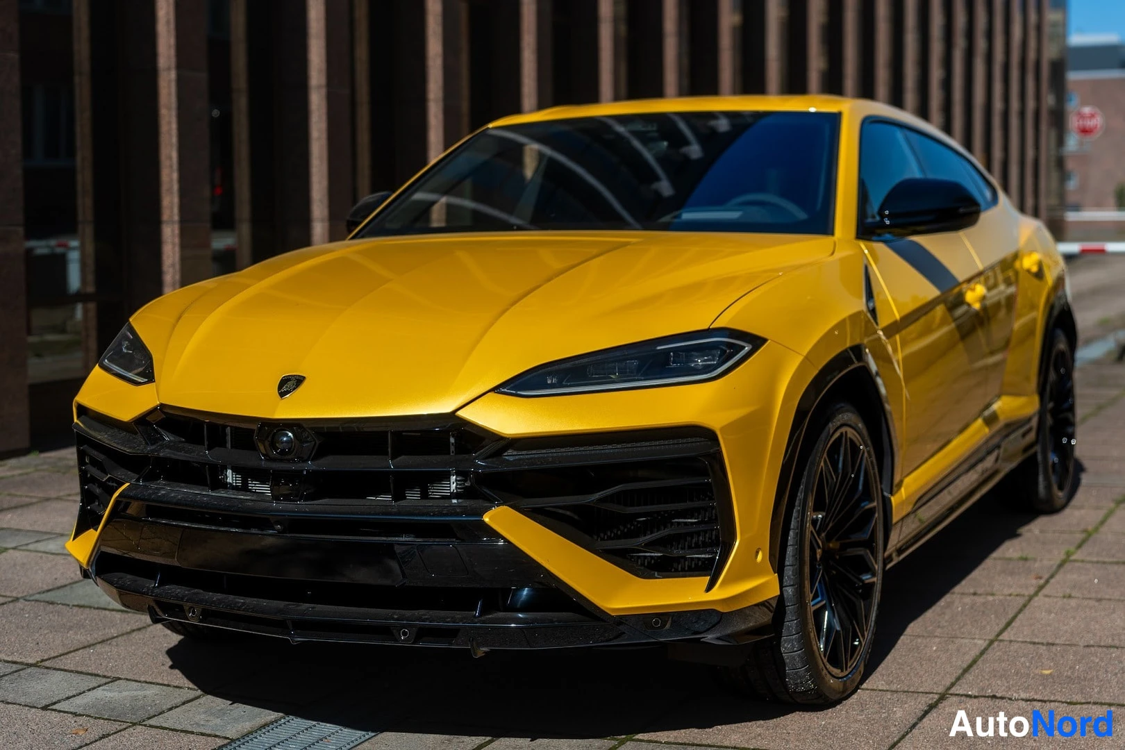Etuviisto, nokka vasemmalle: Keltainen Lamborghini Urus etukulmasta, mustat grille ja keulapuskuri, mustat vanteet.