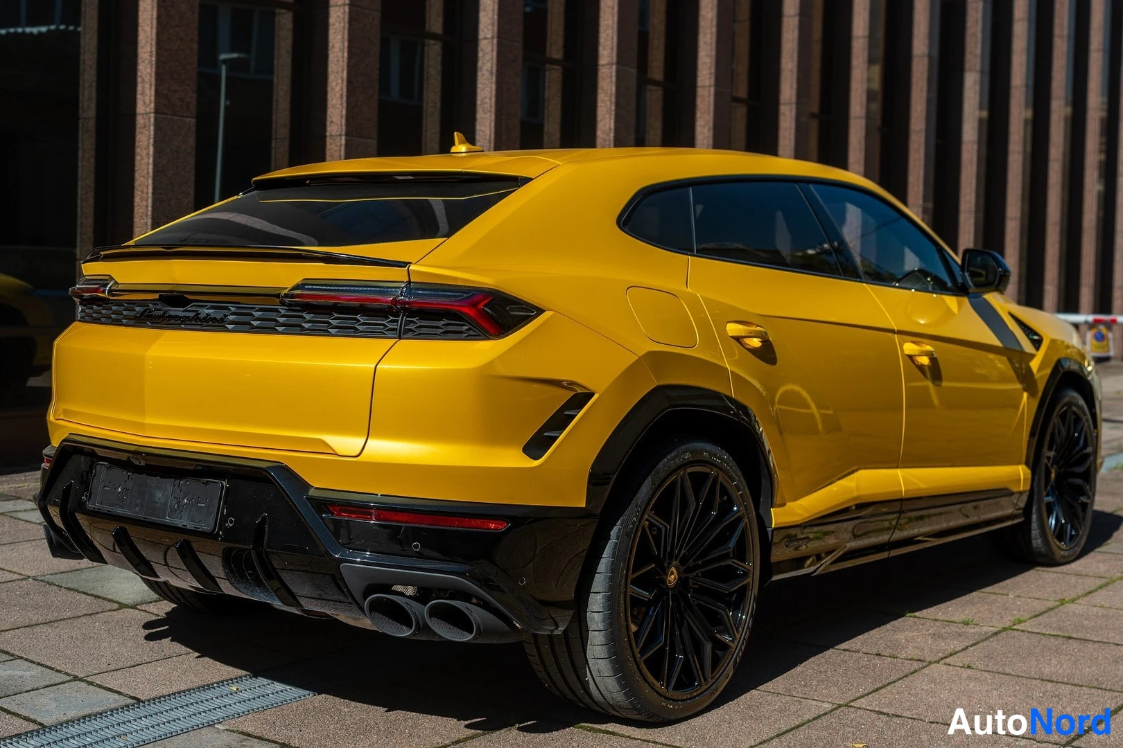 Takaviisto: Keltainen Lamborghini Urus takaviistosta; näkyvät takavalot, mustat vanteet ja kaksi pakoputkea vasemmalla.