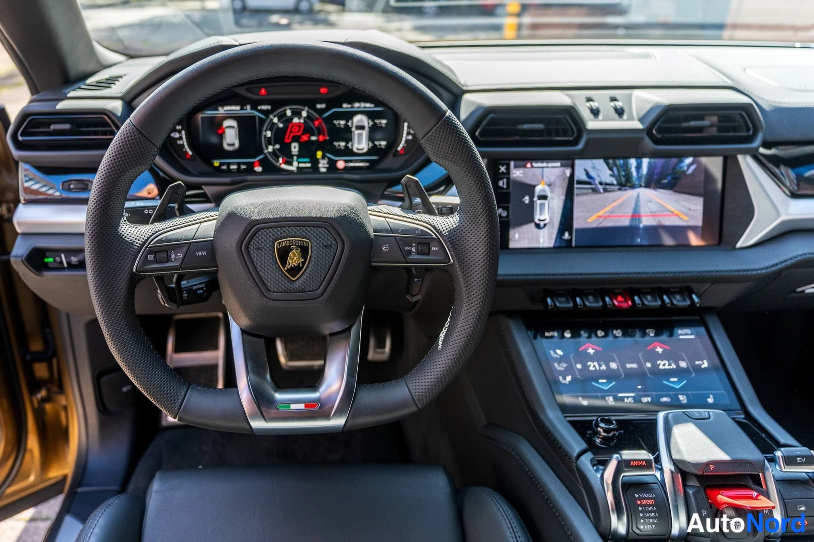 Etuviisto: Ohjaamo kuvattuna kuljettajan paikalta: Lamborghini-ohjauspyörä, digitaalinen mittaristo ja kosketusnäytöt, joiden takakamera ja kauko-ohjattavat toiminnot näky