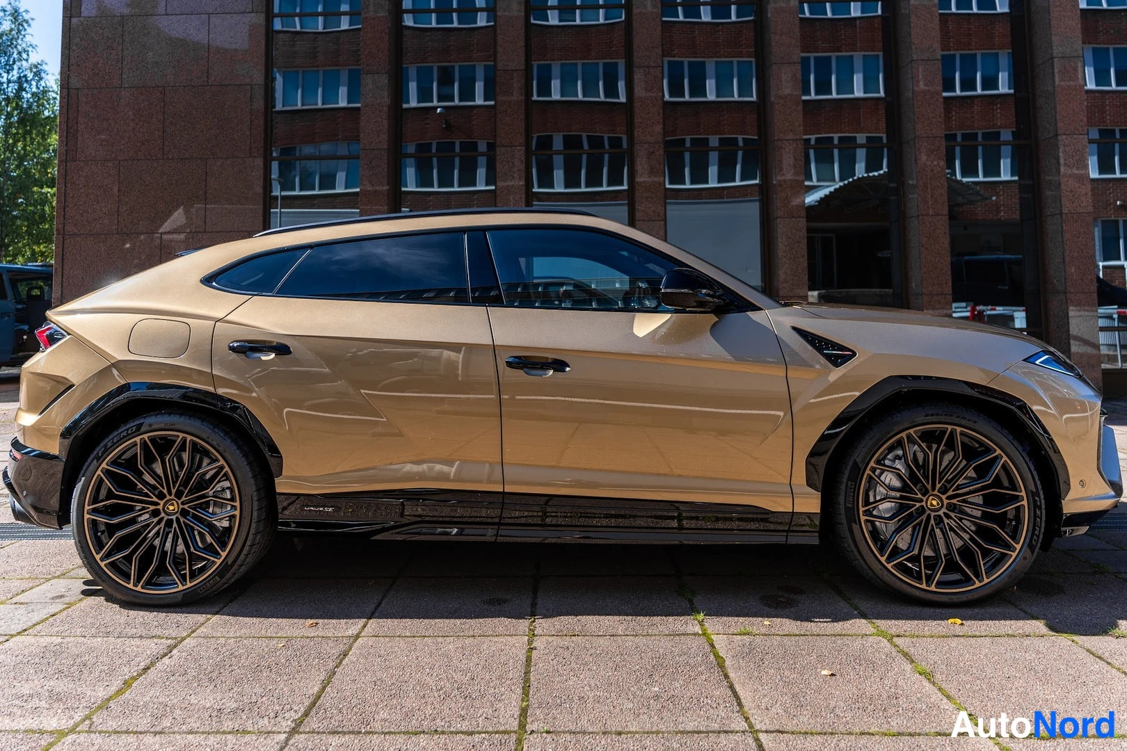 Sivulta: Kullanvärinen Lamborghini Urus sivulta kuvattuna; mustat muoviosat ja pronssihenkiset kevytmetallivanteet.