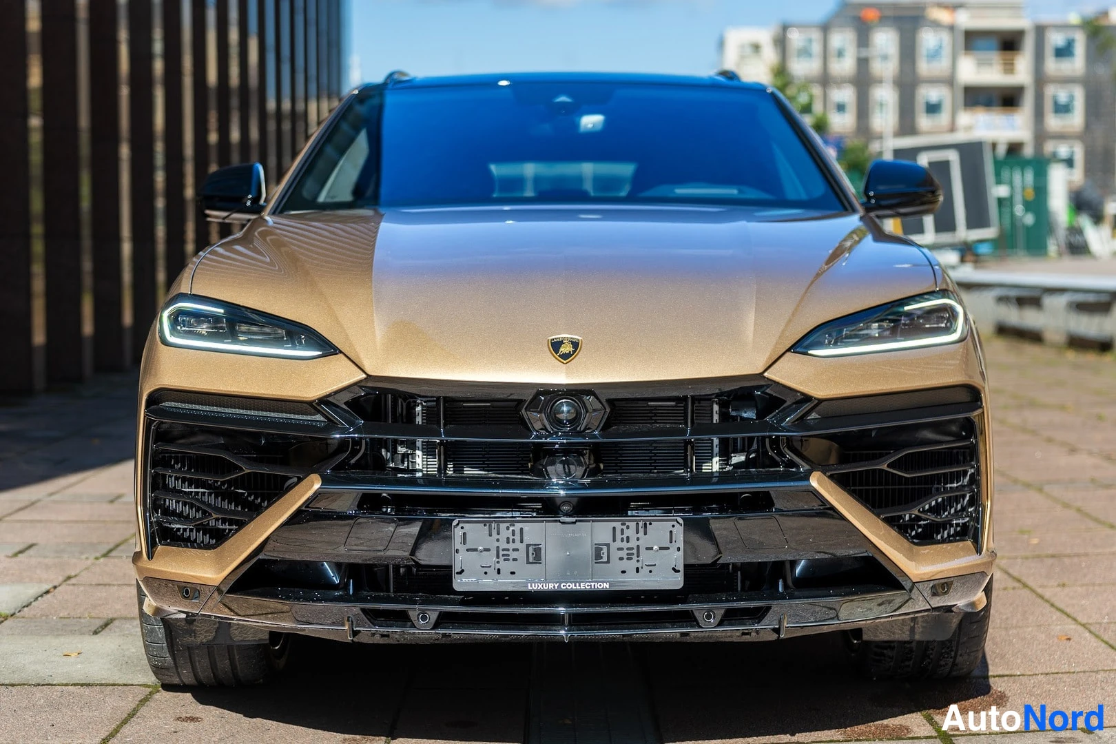 Edestä: Kullanvärinen Lamborghini Urus edestä suoraan kuvattuna; näkyvissä ohut LED-etuvalot, Lamborghini-merkki ja musta etusäleikkö.