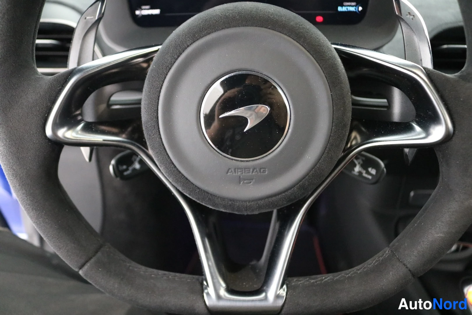 Muu: Lähikuva McLaren-ohjauspyörästä, keskellä AIRBAG-merkintä ja McLaren-logo, mokkanahkapintainen pelta.