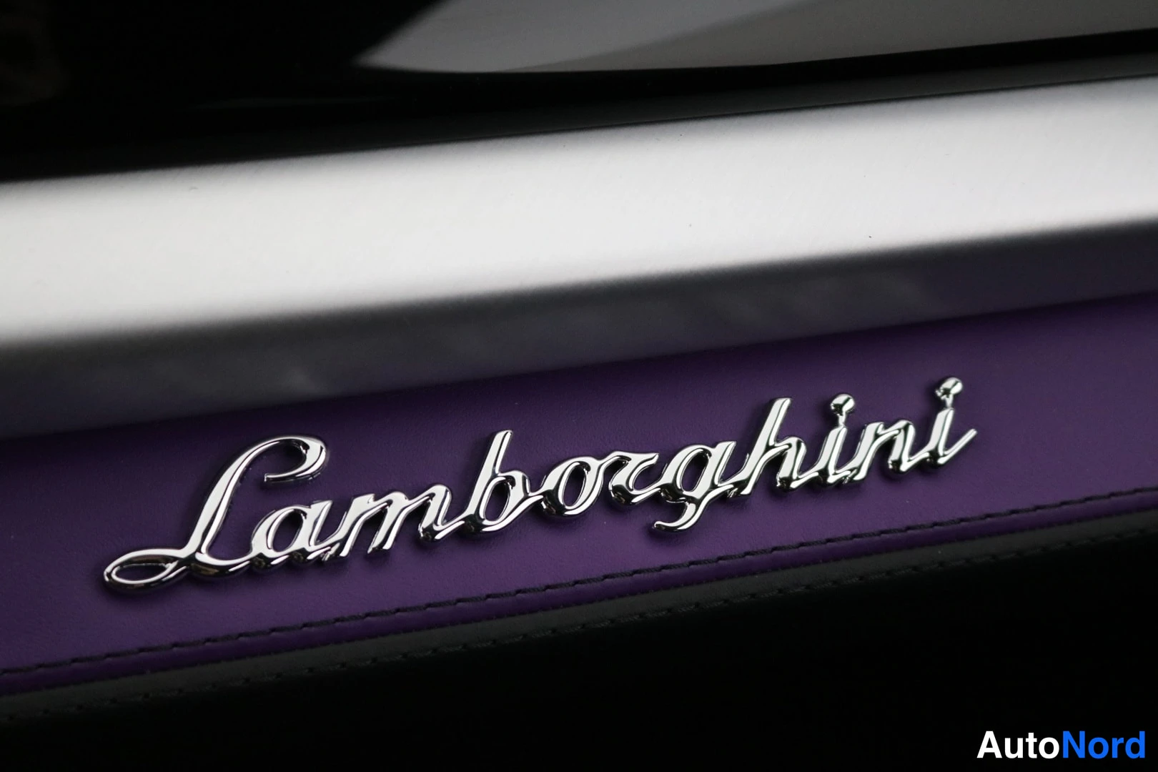 Muu: Lähikuva avattavan oven kynnyksestä: kromattu Lamborghini-kirjoitus violetilla kynnyslistalla ja hopeisen listan alla.