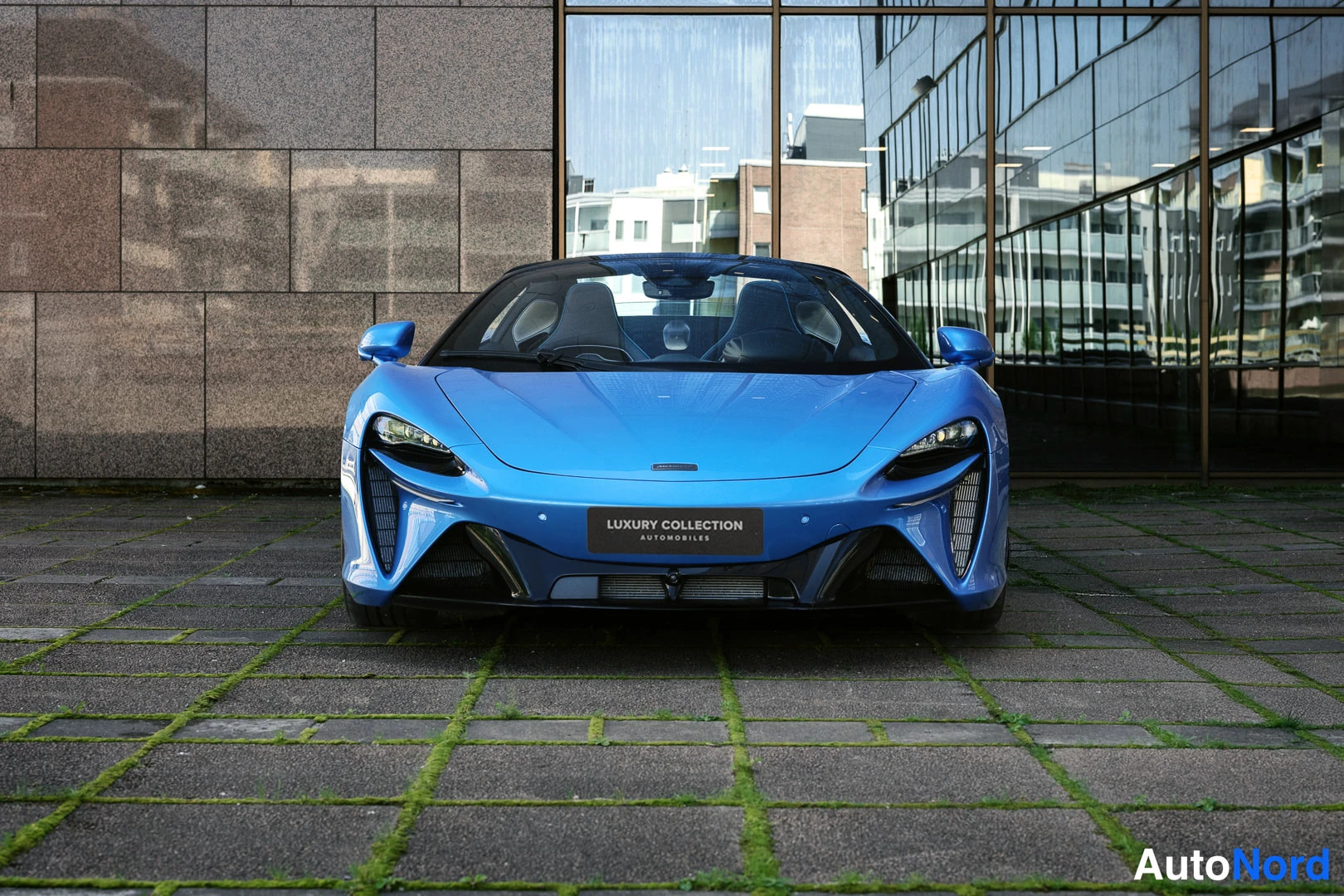 Edestä: Sininen avo-auto suoraan edestä, etusäleiköt ja kojelauta näkyvät
