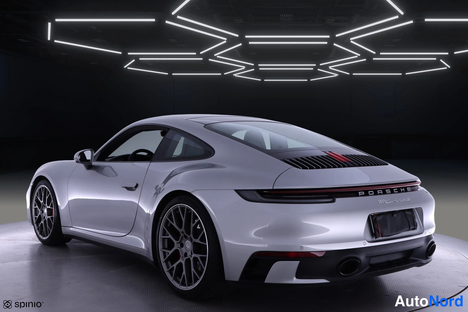 Takaviisto: Porsche 911 -auton takakulma vasemmalta; hopeinen coupé, takavalojen poikittaispalkki, PORSCHE-teksti ja kaksiosaiset pakoputket näkyvät.