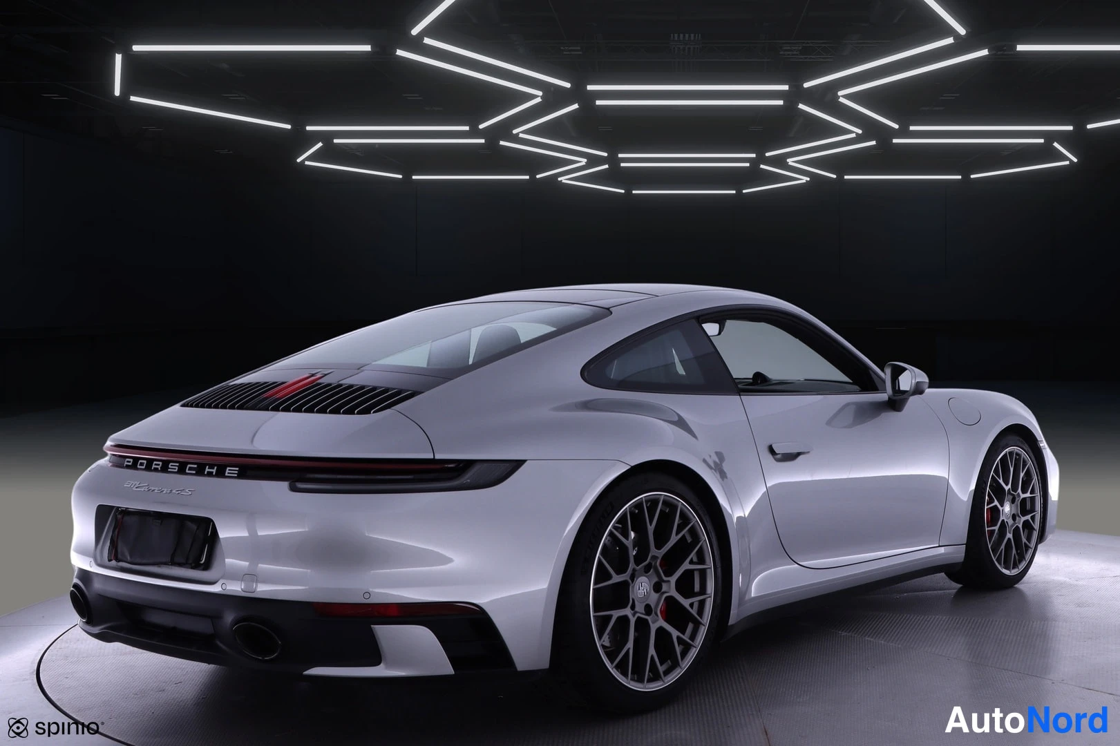 Takaviisto: Porsche 911 -auton takakulma oikealta; hopeinen coupé, PORSCHE-takateksti, moottoritilan ritilä ja kaksi pakoputkea näkyvät.