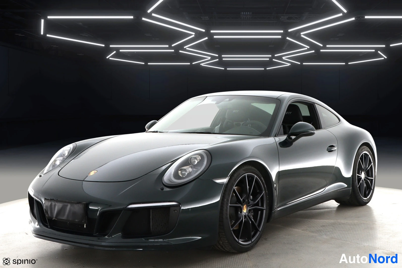 Etuviisto, nokka vasemmalle: Porsche 911 -coupén etukulmatarkastus tummanvihreällä korilla studiovalaistuksessa.