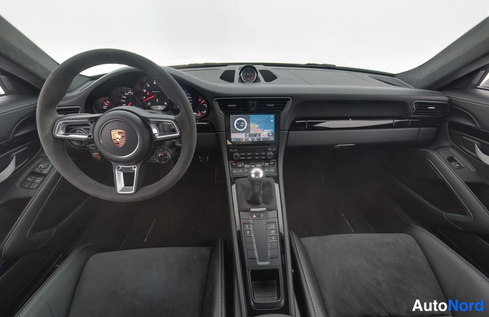 Muu: Autohallissa tummaa sisustaa: mittarit, ohjauspyörä (Porsche), navigointinäyttö, manuaalivaihto ja penkit.