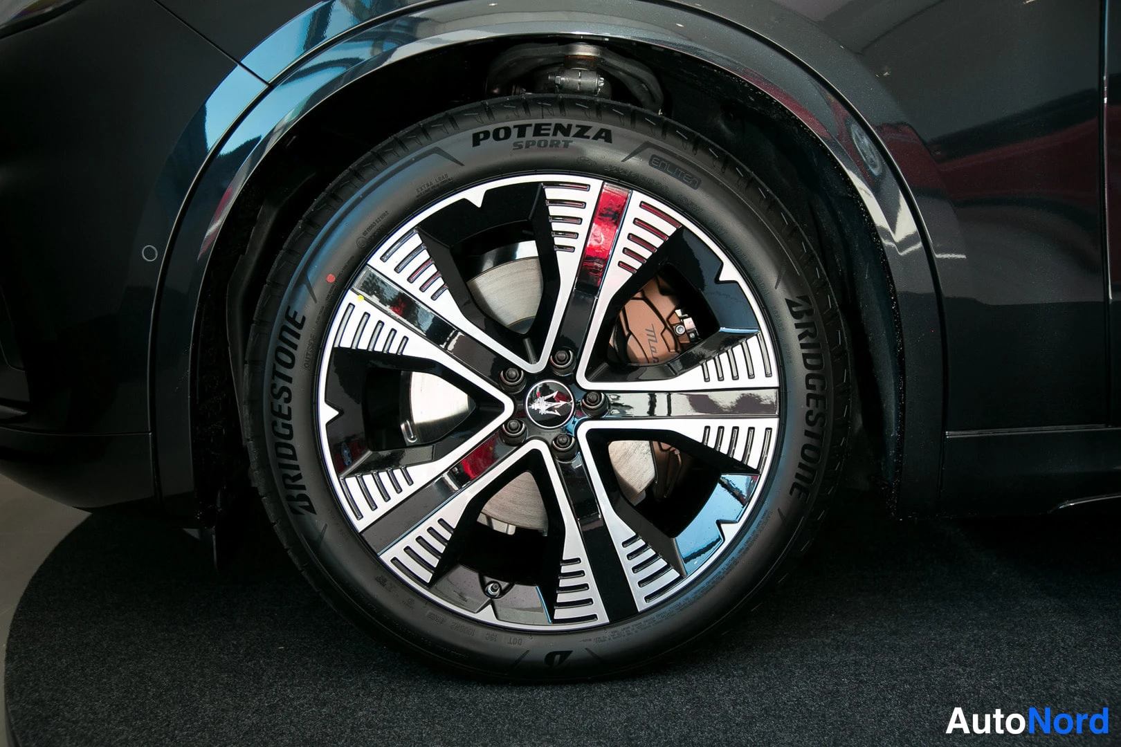 Sivulta: Lähikuva mustan auton takapyörästä Bridgestone Potenza Sport -rengalla ja kaksivärisellä vanteella.