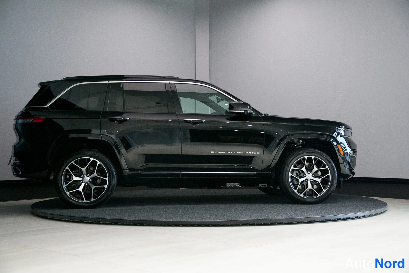 Sivulta: Mustan Jeep Grand Cherokee -maasturin sivunäkymä, GRAND CHEROKEE -teksti ovessa, monihaaravanteet ja kattokaiteet.