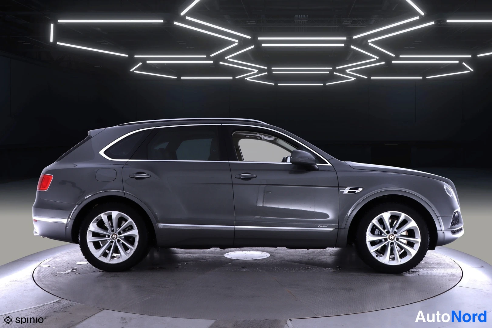 Etuviisto, nokka oikealle: Auton etukulma kuvattuna oikealta: harmaa Bentley Bentayga -maasturi studiovalaistuksessa alustalla.