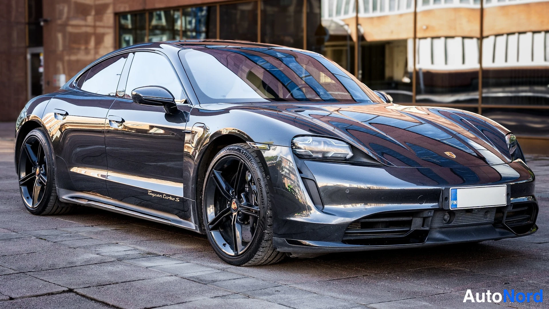 Etuviisto, nokka oikealle: Tummansinertävä Porsche Taycan Turbo S -sedan edusta ja vasen sivu kolmasosa-kulmasta, mustat levyt.
