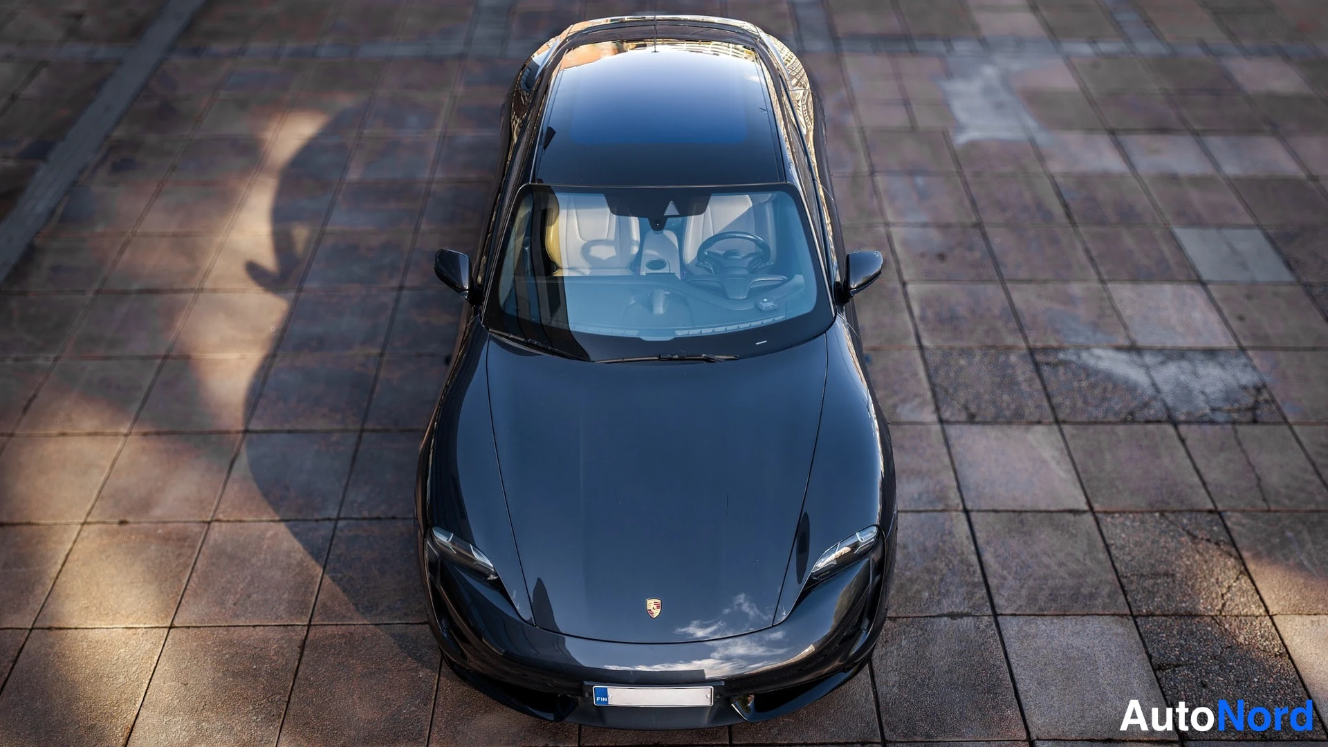 Edestä: Yläkulma kuvattu Porsche Taycanin konepellille: tuulilasi, kattopaneeli ja etusälekaito näkyvät suoraan ylhäältä, auton keskuslukon kohokilpi konepellillä.