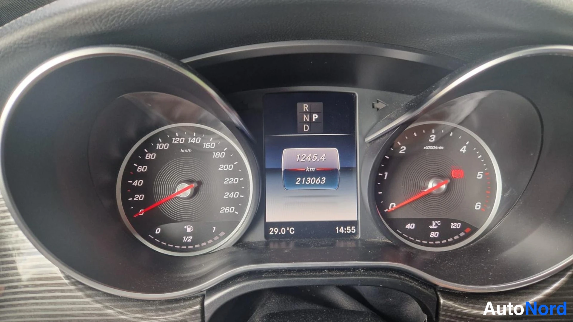 Yksityiskohta: Mercedes-Benzin mittaristo: nopeusmittari ja kierrosmittari, keskellä näyttö, jossa lukemat 1245,4 km, 213063 km, 29,0 °C ja 14:55; vaihdenäyttö P/R/N/D.