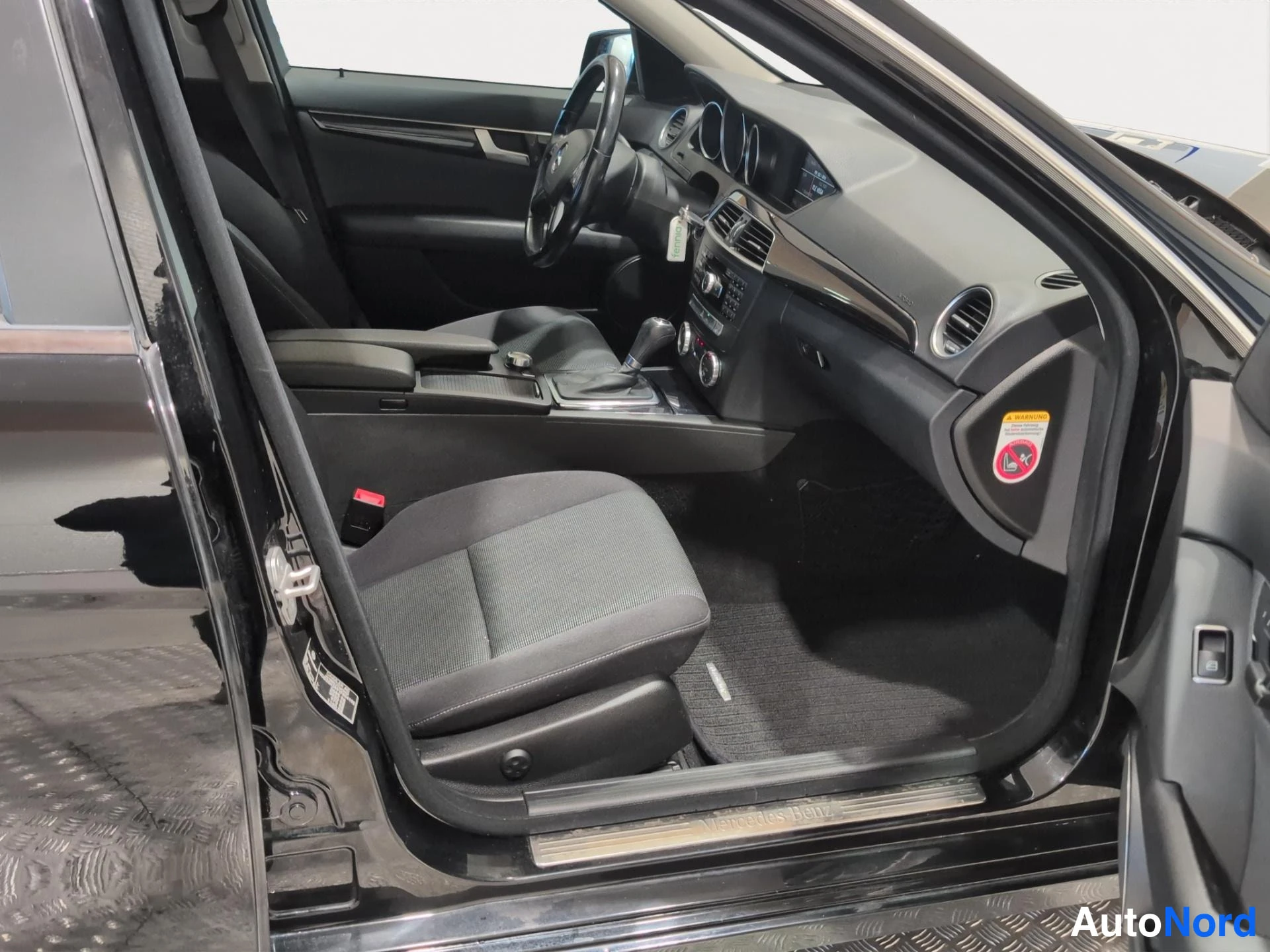 Edestä: Mercedes-Benzin avattu kuljettajan oven sivusta kuvattu sisätila: kangasistuin, käsijarru, keskikonsoli ja kojelauta näkyvissä.