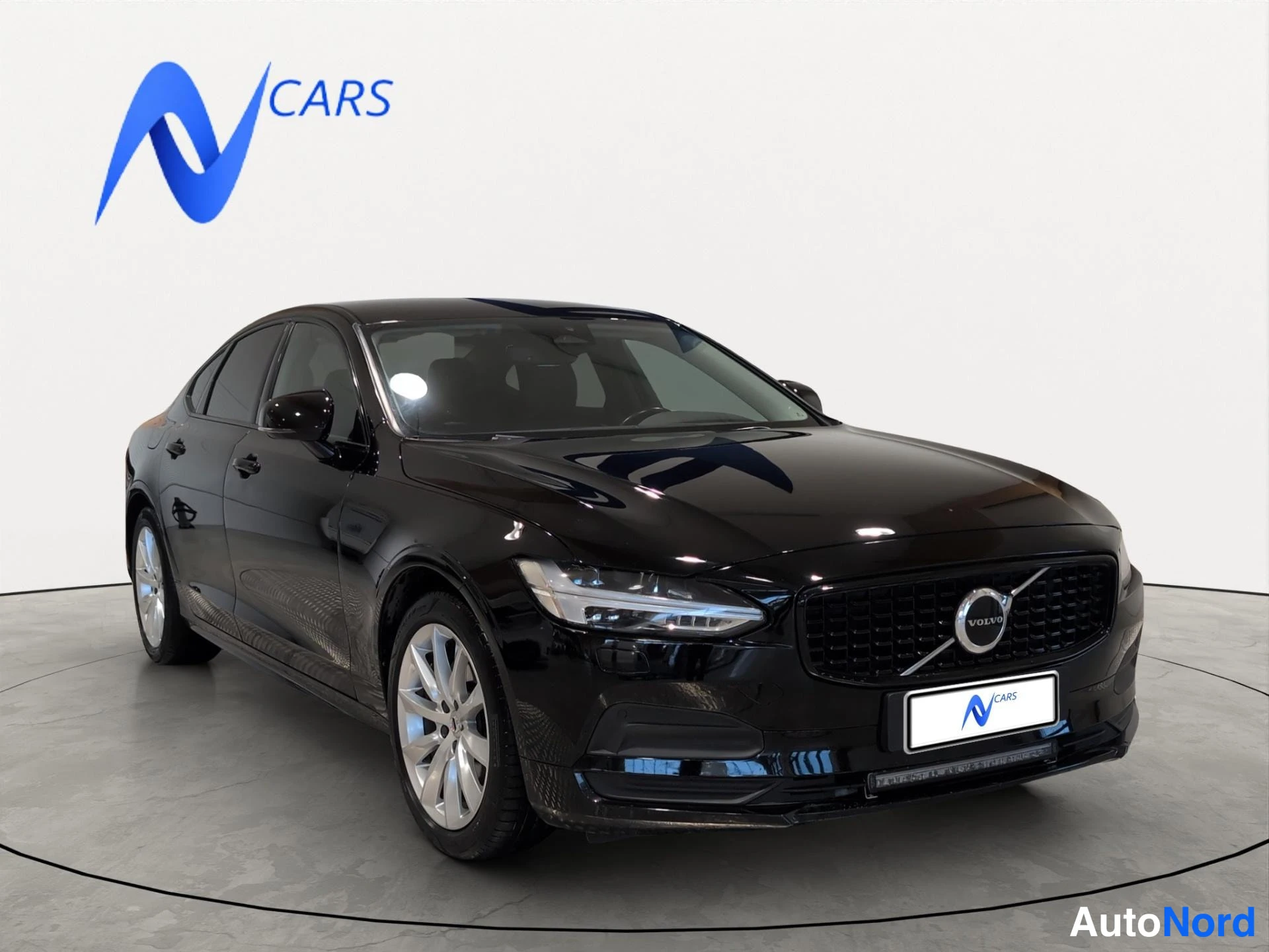 Etuviisto, nokka oikealle: Musta Volvo S90 -sedan etuviistosta vasemmalta kuvattuna; Volvo-merkki säleikössä ja hopeiset vanteet.
