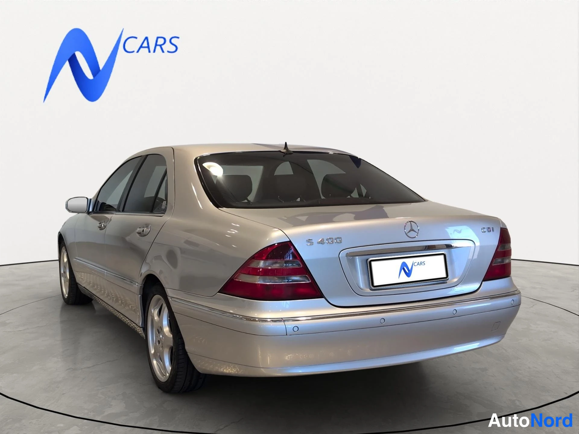Takaviisto: Hopeansävyinen Mercedes-Benz S-luokan sedan takakulmasta vasemmalta kuvattuna, takavalojen ja merkin näkyvä.