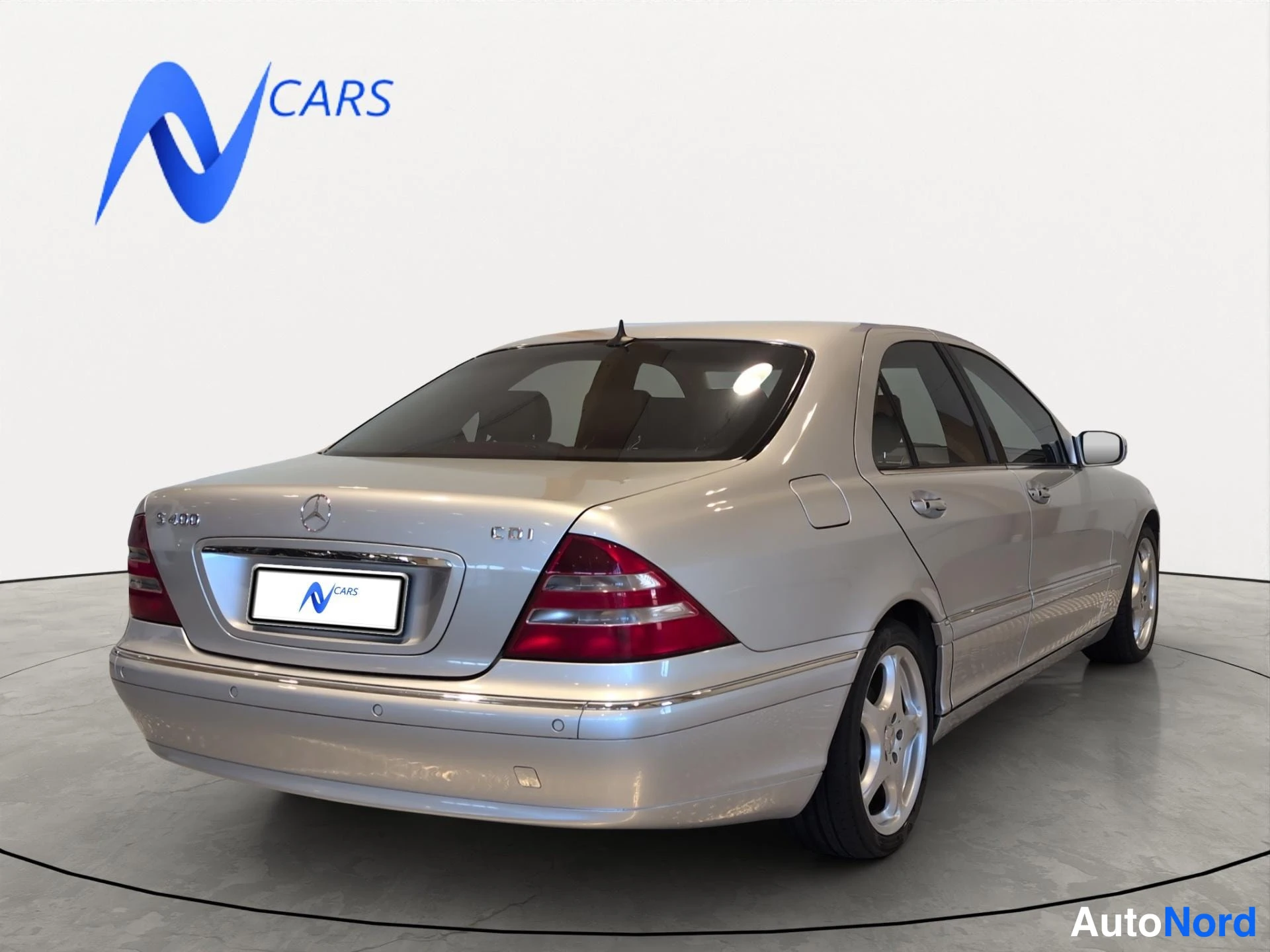 Takaviisto: Hopeansävyinen Mercedes-Benz S-luokan sedan takakulmasta oikealta kuvattuna, takavalojen ja korin reunat näkyvät.