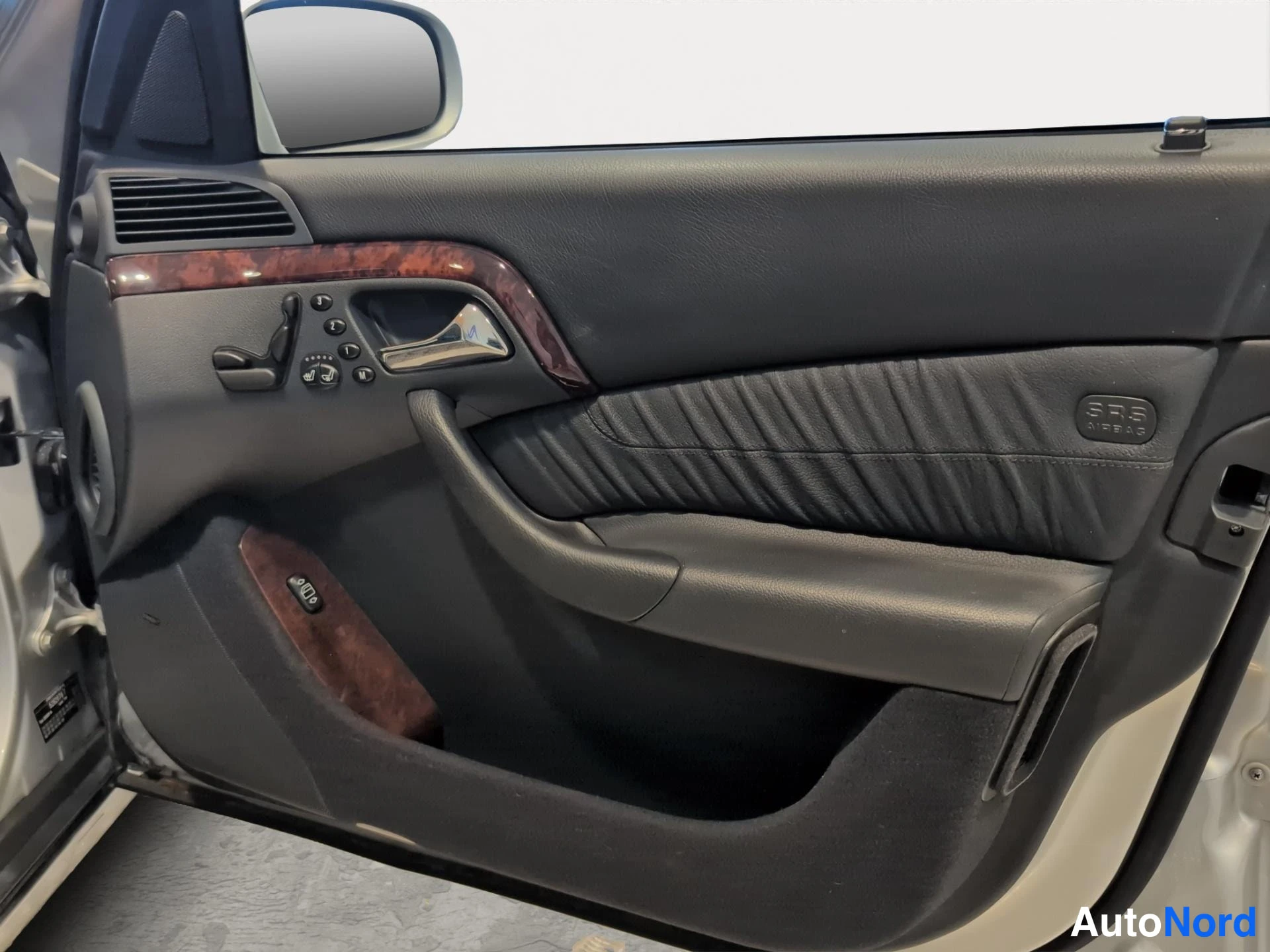Muu: Mercedes-Benzin auton kuljettajan ovi auki näkyvä sisäpelti: sähköikkunan nappulat, puukoriste ja SRS-airbag-merkintä.