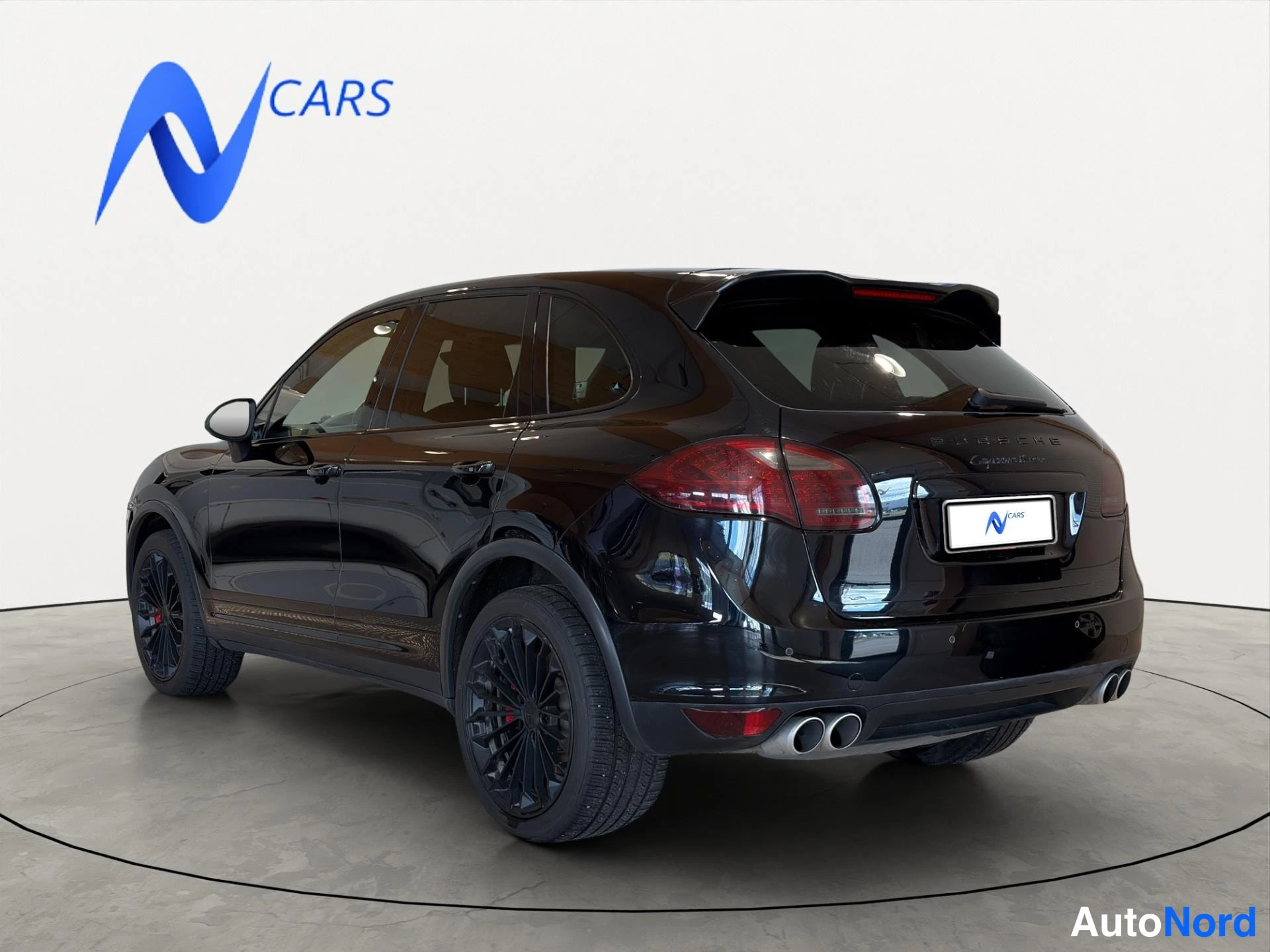 Takaviisto: Musta Porsche Cayenne kuvattuna takaa vasemmalta; takakori, takavalot, neljä pakoputkea ja mustat vanteet näkyvät.