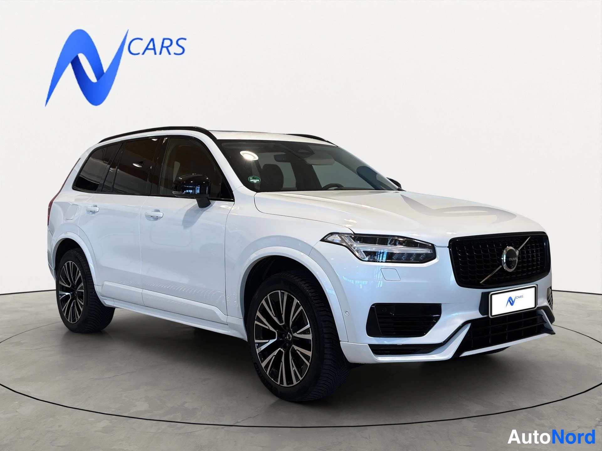 Etuviisto, nokka oikealle: Valkoinen Volvo XC90 -maasturi vinosti edestä oikealta kuvattuna studiotaustaa vasten.