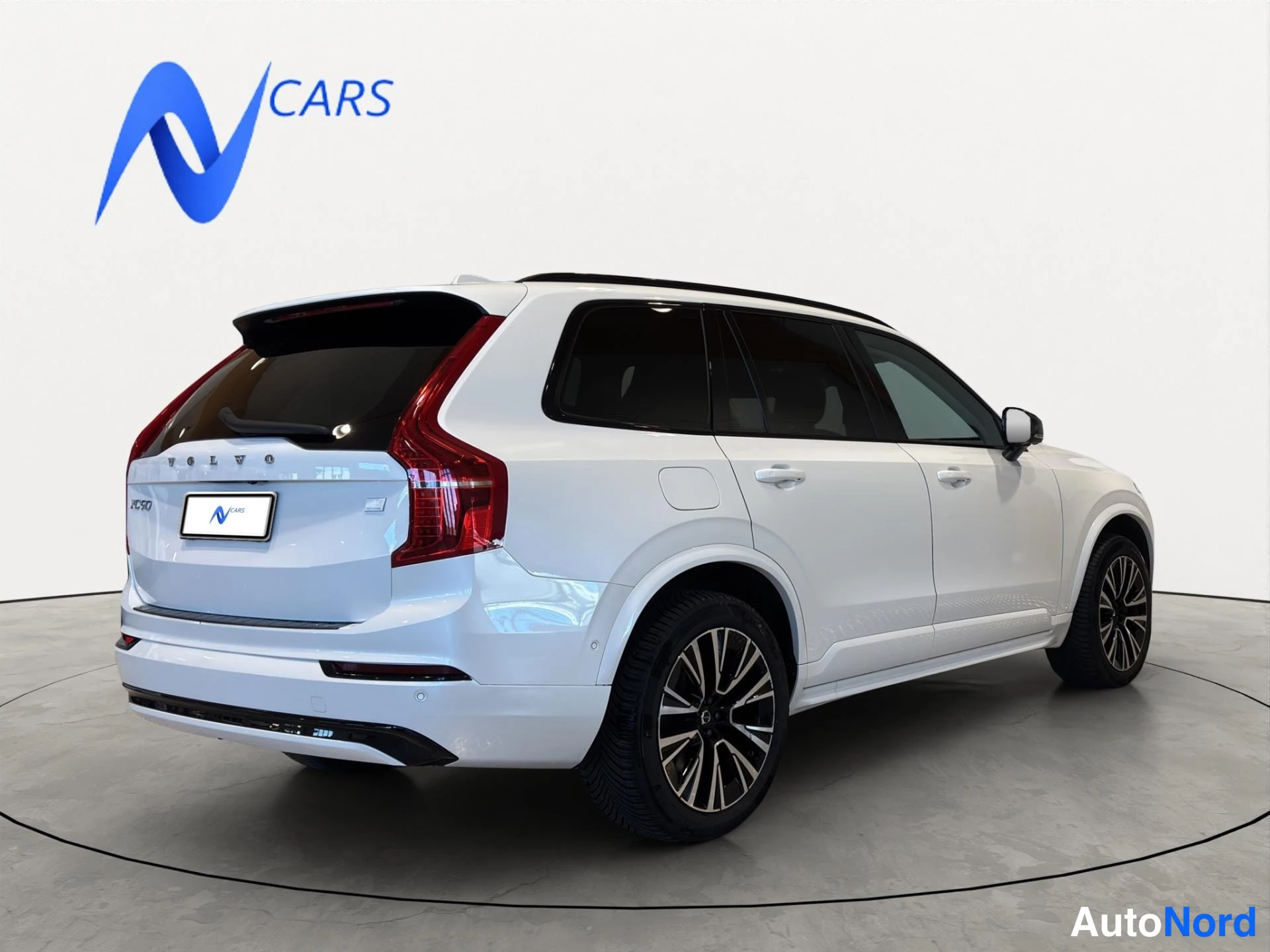 Takaviisto: Valkoisen Volvo XC90:n takapää ja vasen sivu kuvattuna studiotaustaa vasten.