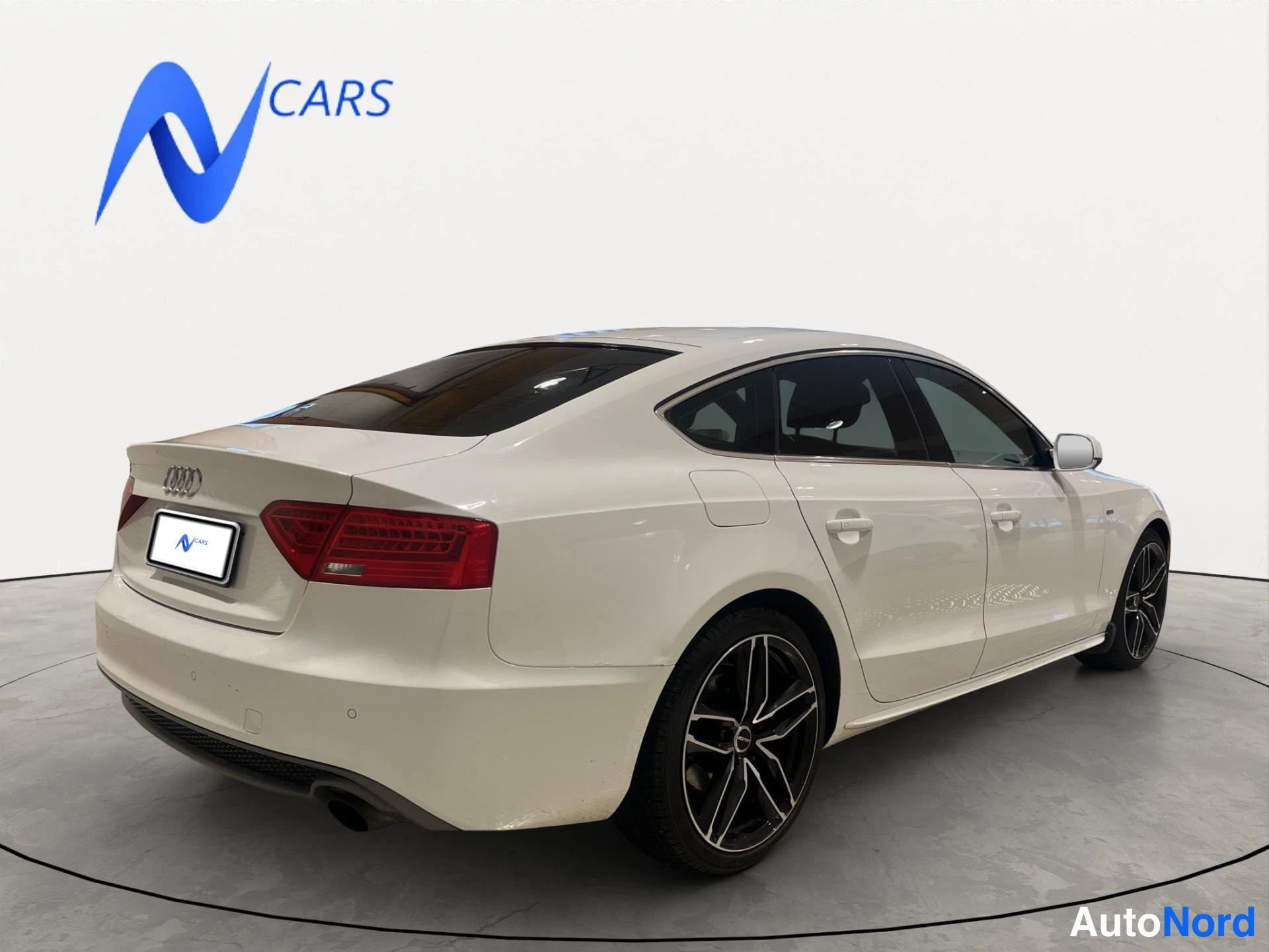 Takaviisto: Valkoisen Audi A5 Sportbackin takakulma, punaiset takavalot ja mustat vanteet, N Cars -logo taustalla.