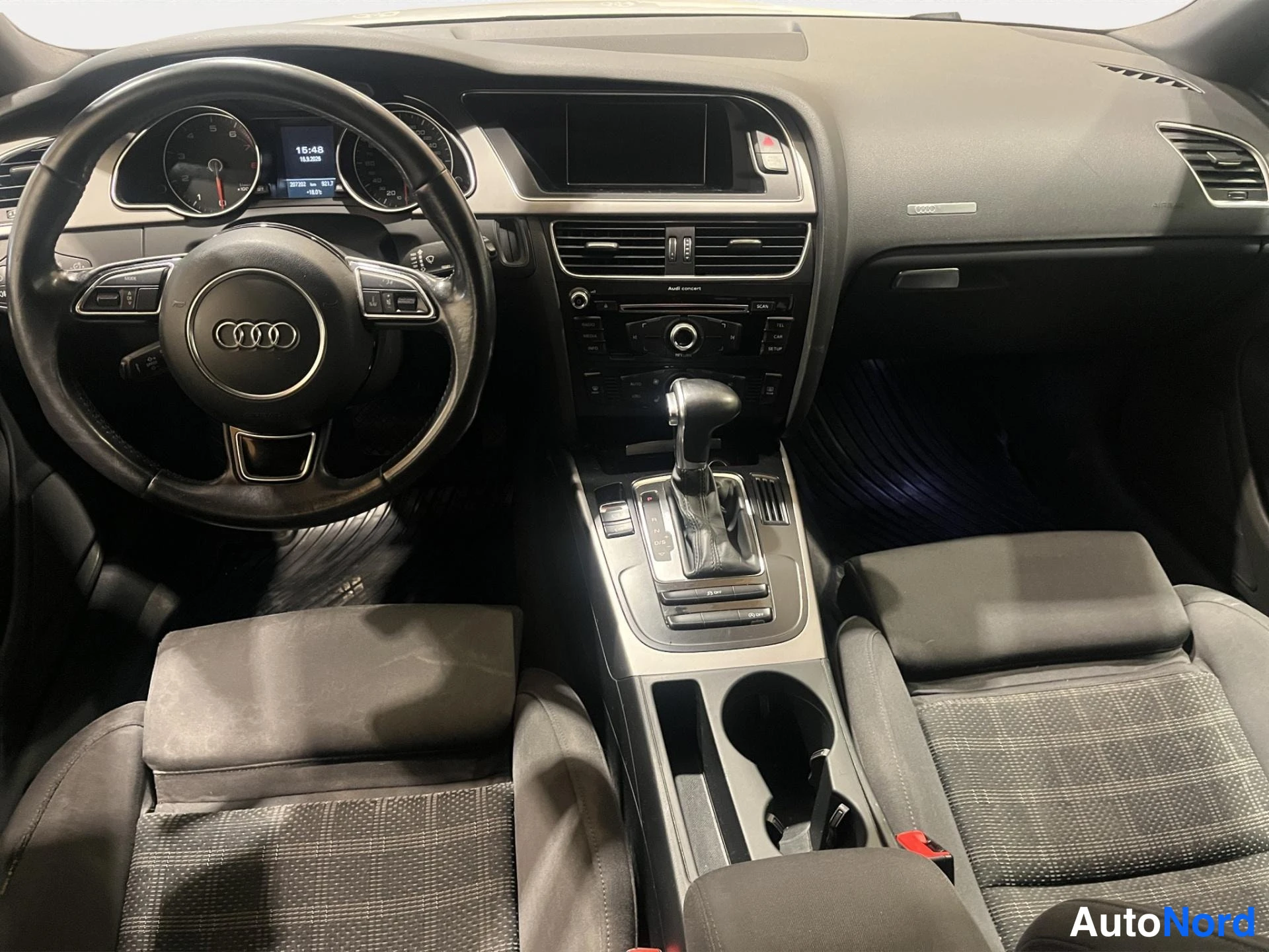 Muu: Ohjaamo etupyörän suunnasta: Audi-ohjauspyörä, mittaristo, radio ja automaattivaihteiston valitsin.