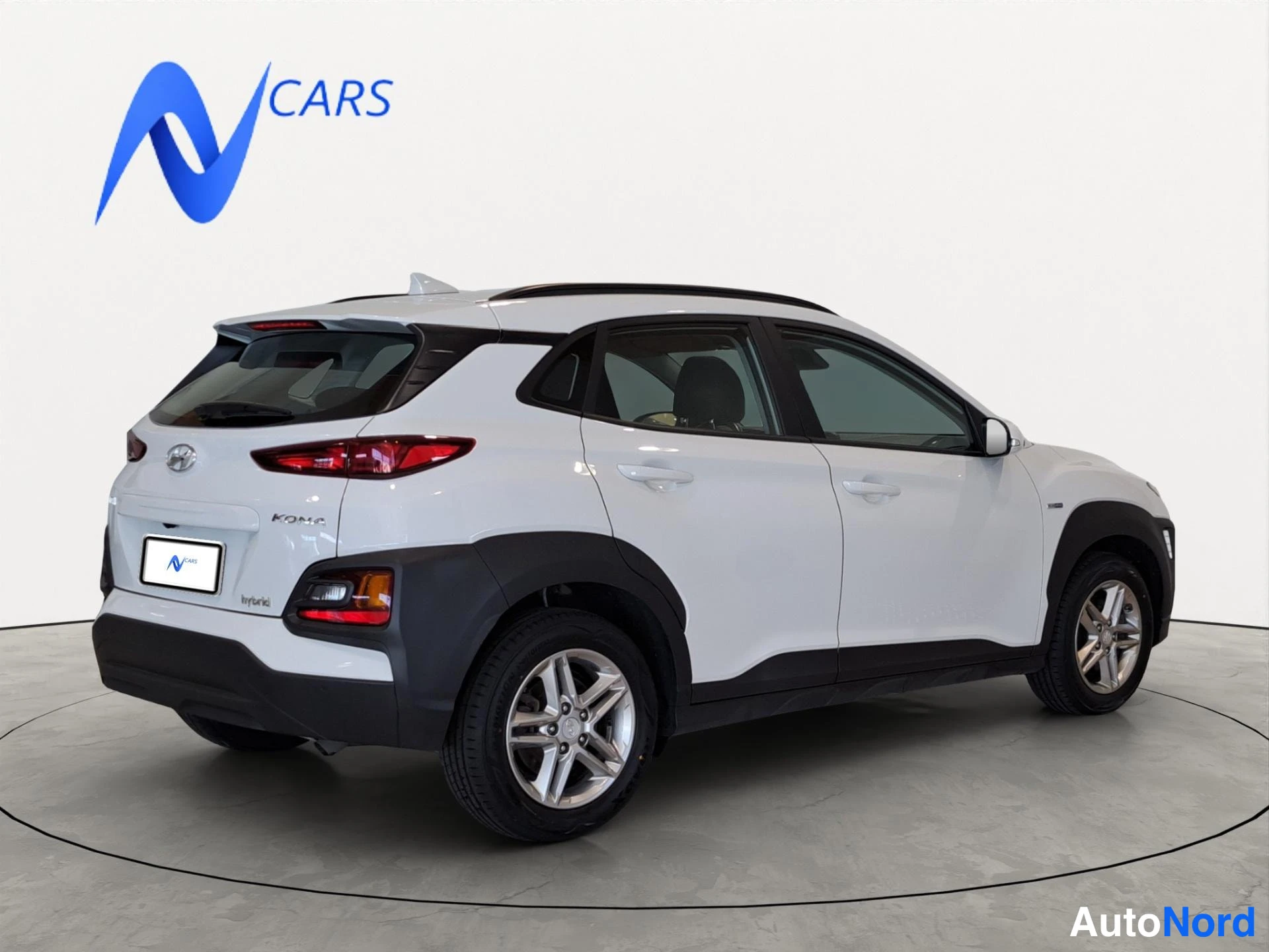 Takaviisto: Hyundai Kona -maastauton taka- ja sivuprofiili valkoisena, peräosa ja KONA-merkintä näkyvät, kun auto on studioharmaalla alustalla.