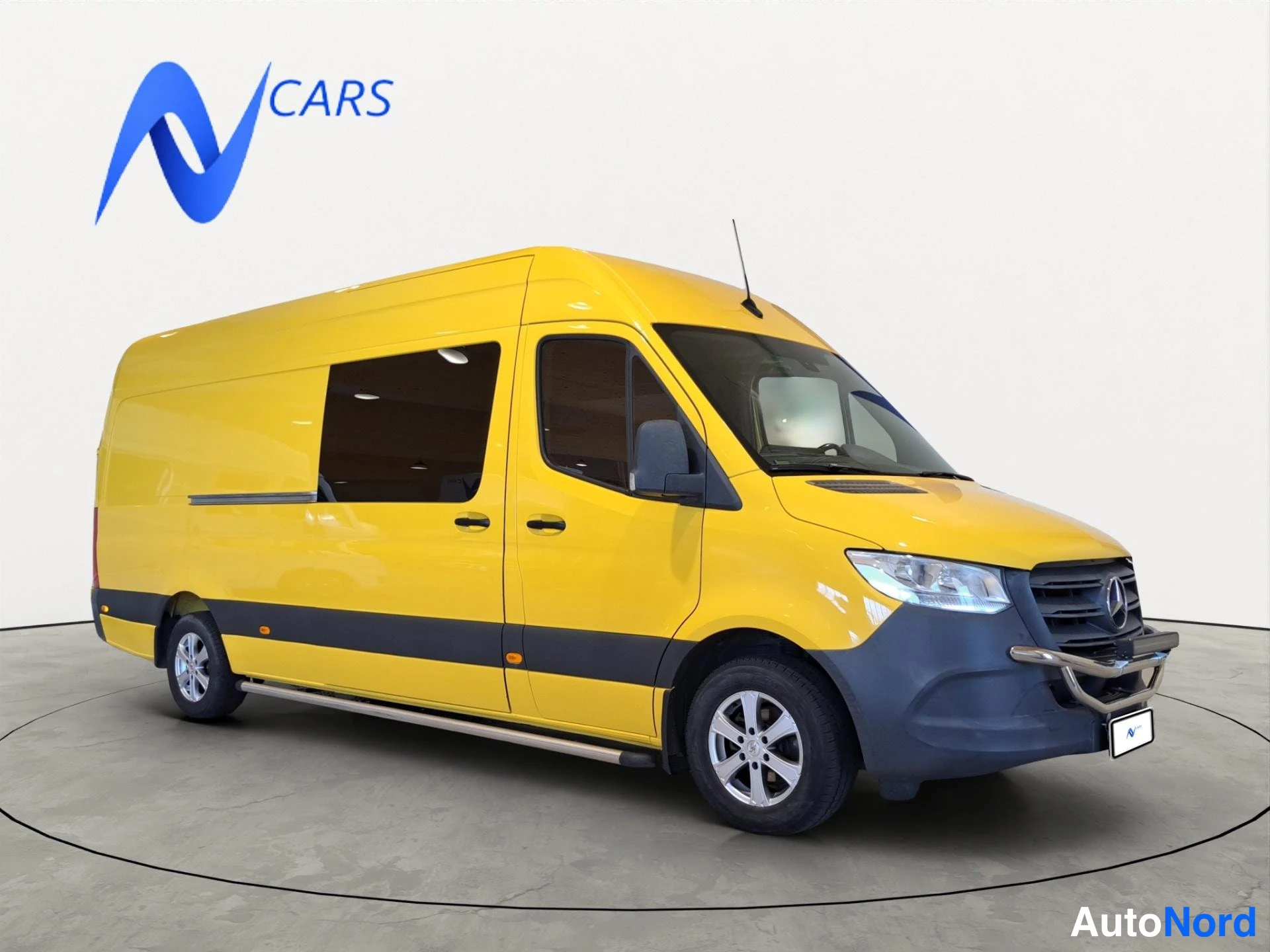 Etuviisto, nokka oikealle: Mercedes-Benz Sprinter -pakettiauto keltaisella korilla kuvattu kolmannelta etukulmalta, keula kuvan oikeassa reunassa.