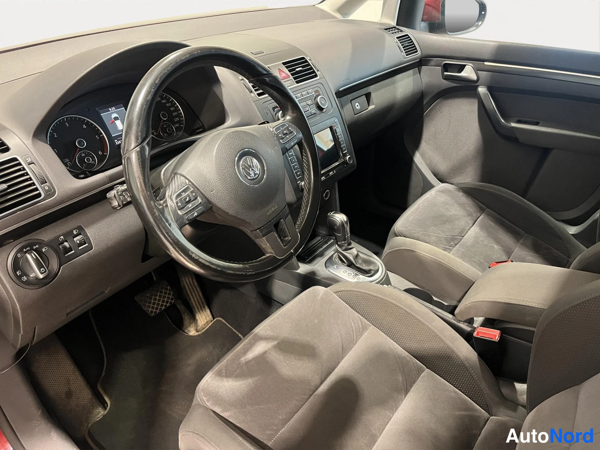Muu: Ohjaamo kuljettajan puolelta: Volkswagen-ohjauspyörä, mittaristo, manuaali-automaattivaihtajan vivut ja tummat kangasistuimet.