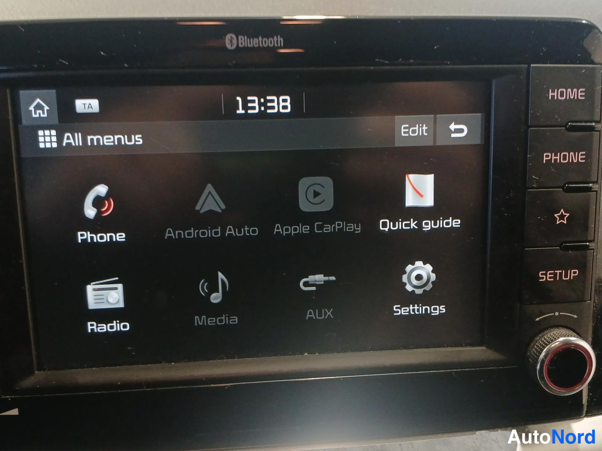 Yksityiskohta: Auton radio/infotainment-näyttö jossa valikot Phone, Android Auto, Apple CarPlay, Radio, Media, AUX ja Settings, Bluetooth-merkintä paneelissa.