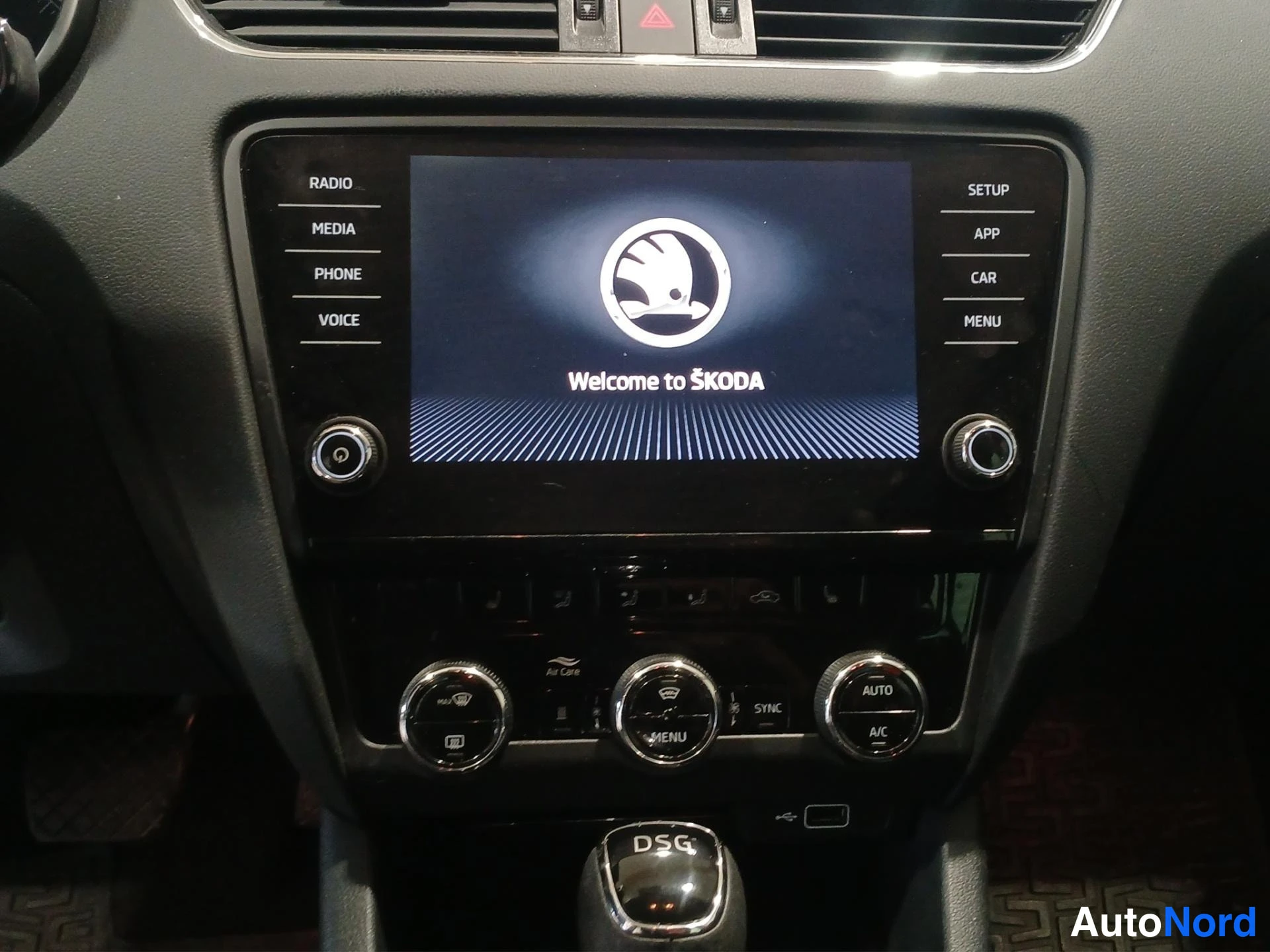 Yksityiskohta: Kojelaudan keskiosa: ŠKODA-näyttö, jossa teksti 'Welcome to ŠKODA' ja valikot RADIO, MEDIA, PHONE, VOICE, SETUP, APP, CAR, MENU; alla automaattisen ilmastoinnin
