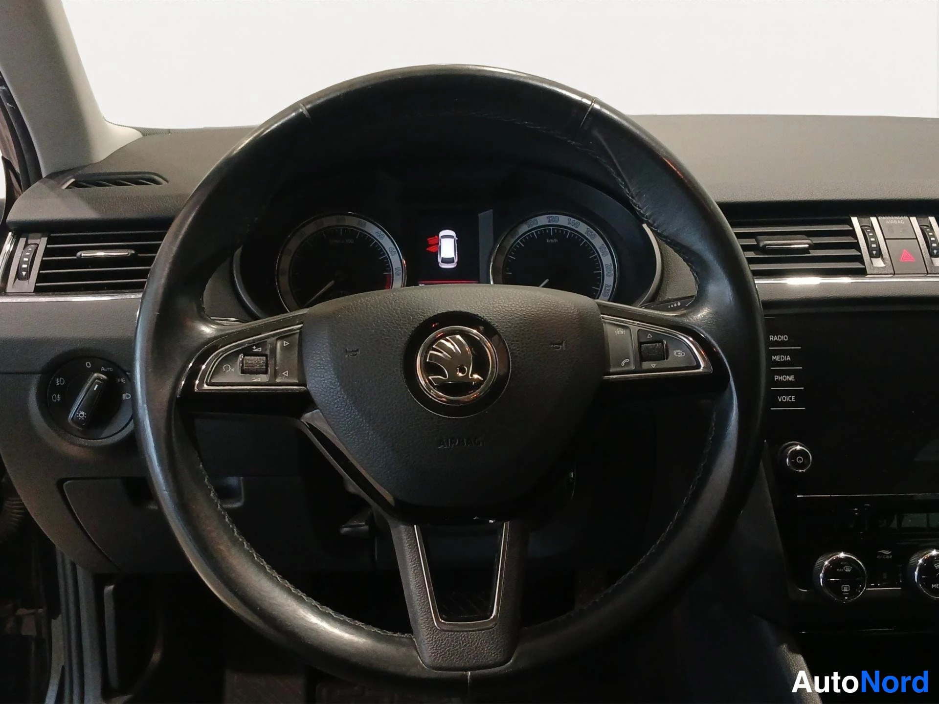 Yksityiskohta: Ohjauspyörä ja mittaristo edestä: ŠKODA-logo ohjauspyörässä, monitoiminnappulat, takaosassa radiovalikot RADIO, MEDIA, PHONE, VOICE.