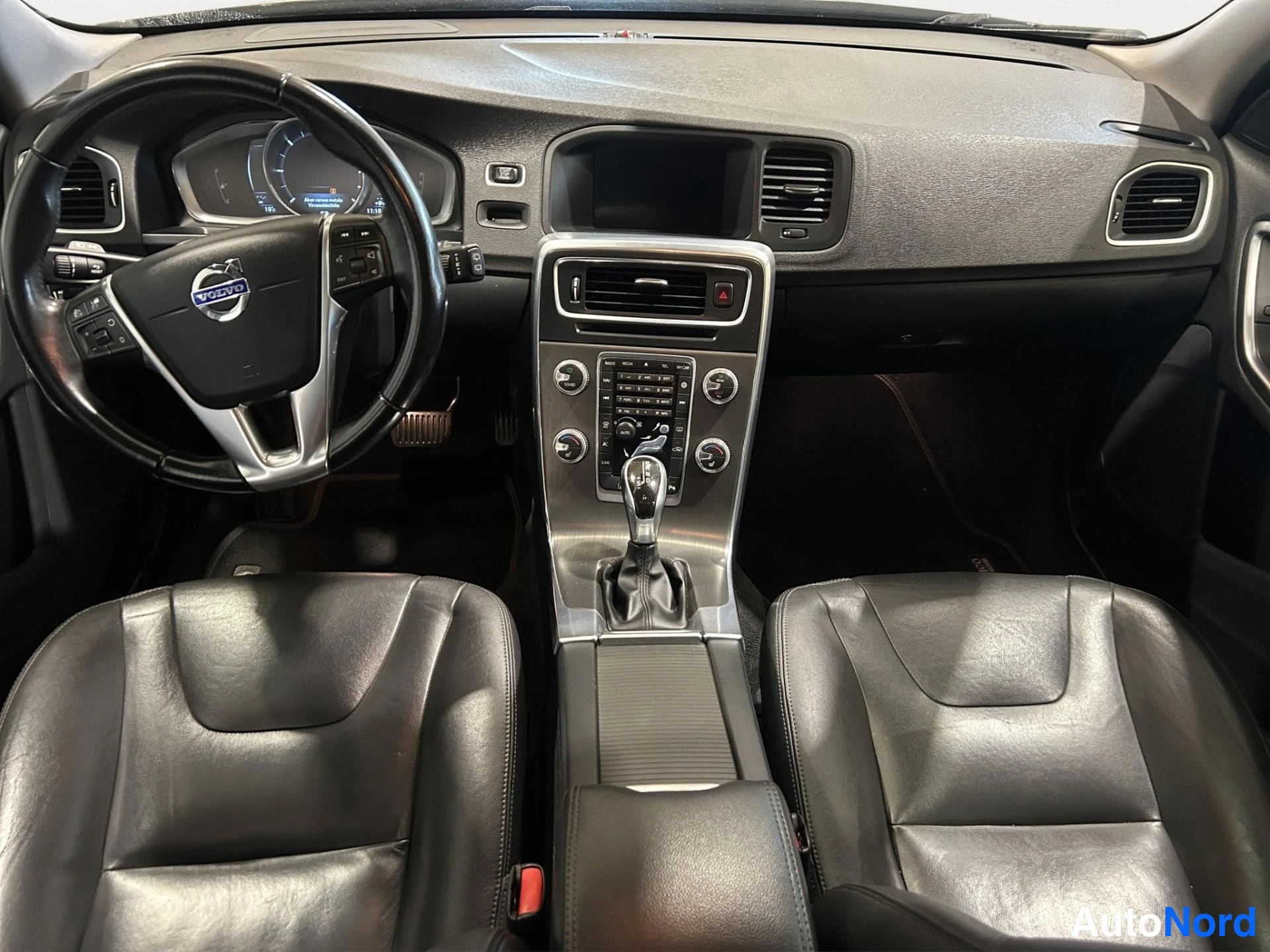Muu: Volvo V60:n sisätilat: ohjauspyörä, kojelauta, automaattivaihteen valitsin ja kaksi mustaa nahkaistuinta.