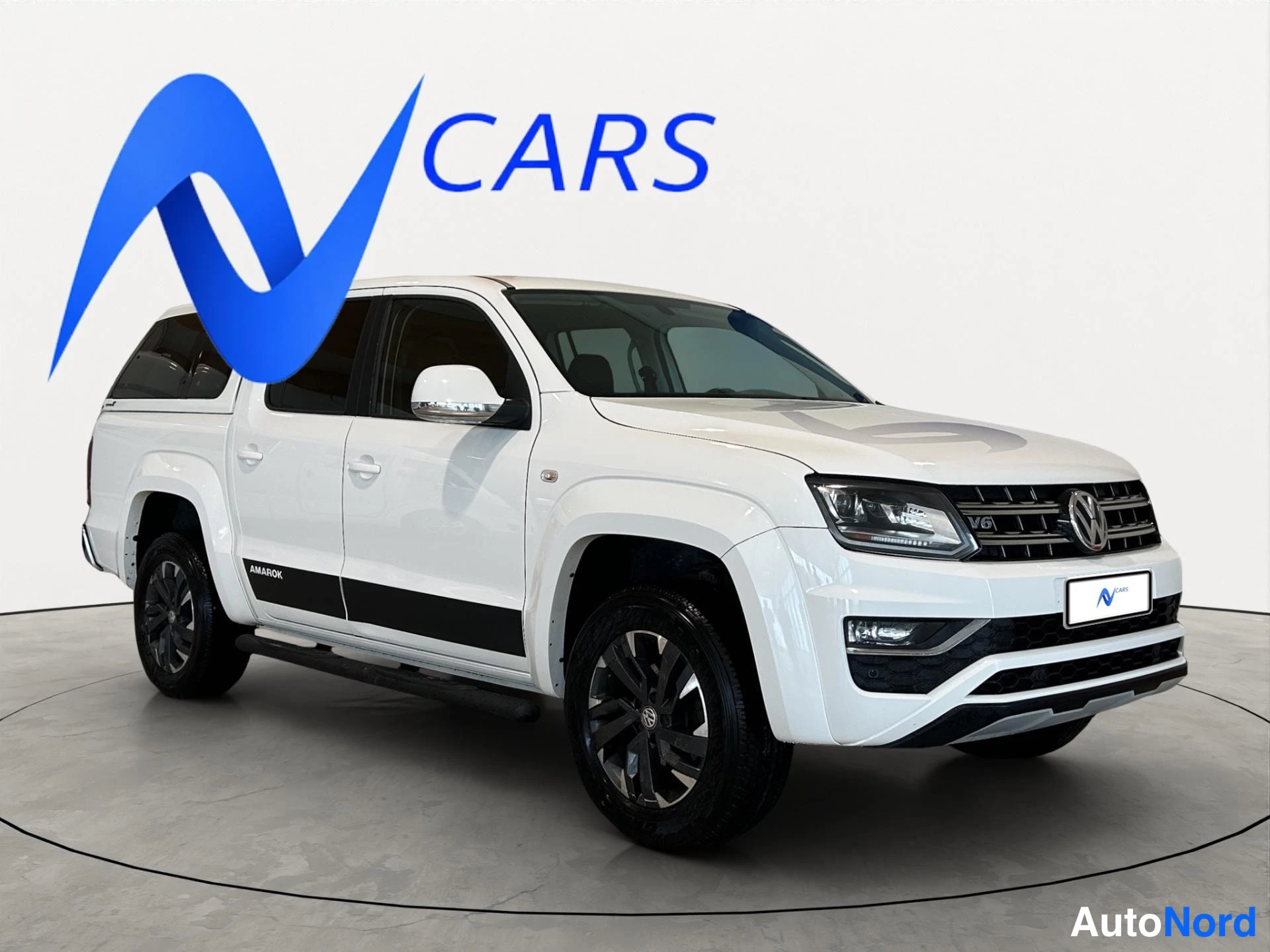 Etuviisto, nokka oikealle: Valkoinen Volkswagen Amarok -nappakuorma-auto kolmasosan etukuvaan, keula oikealla.